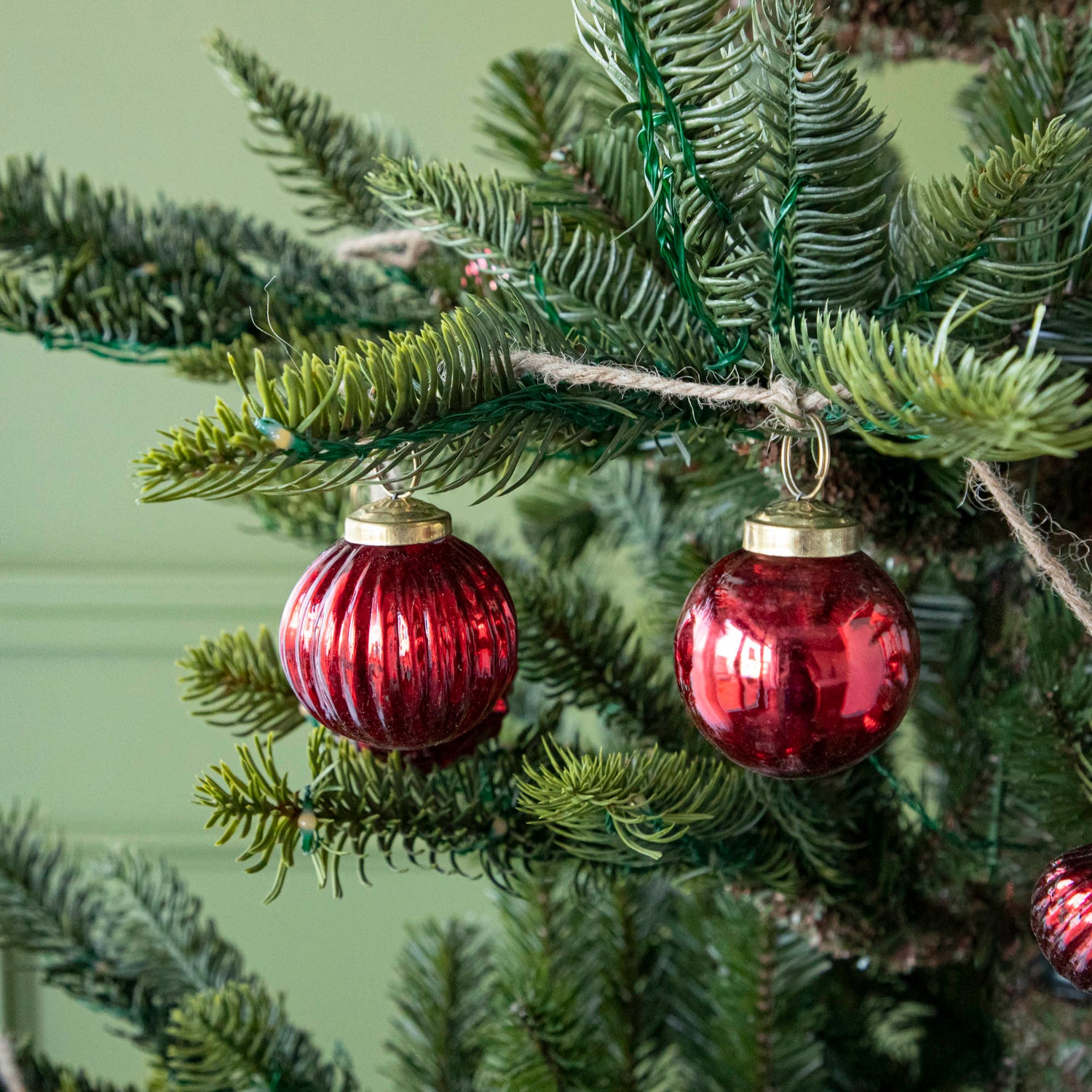 A close up of two Embossed Red Mercury Glass Ornaments showing the detailing and jute cord hanging on a tree.