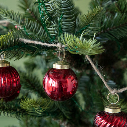 A close up of three Embossed Red Mercury Glass Ornaments showing the detailing and jute cord hanging on a tree.