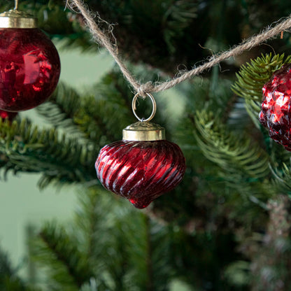 A close up of three Embossed Red Mercury Glass Ornaments showing the detailing and jute cord hanging on a tree.