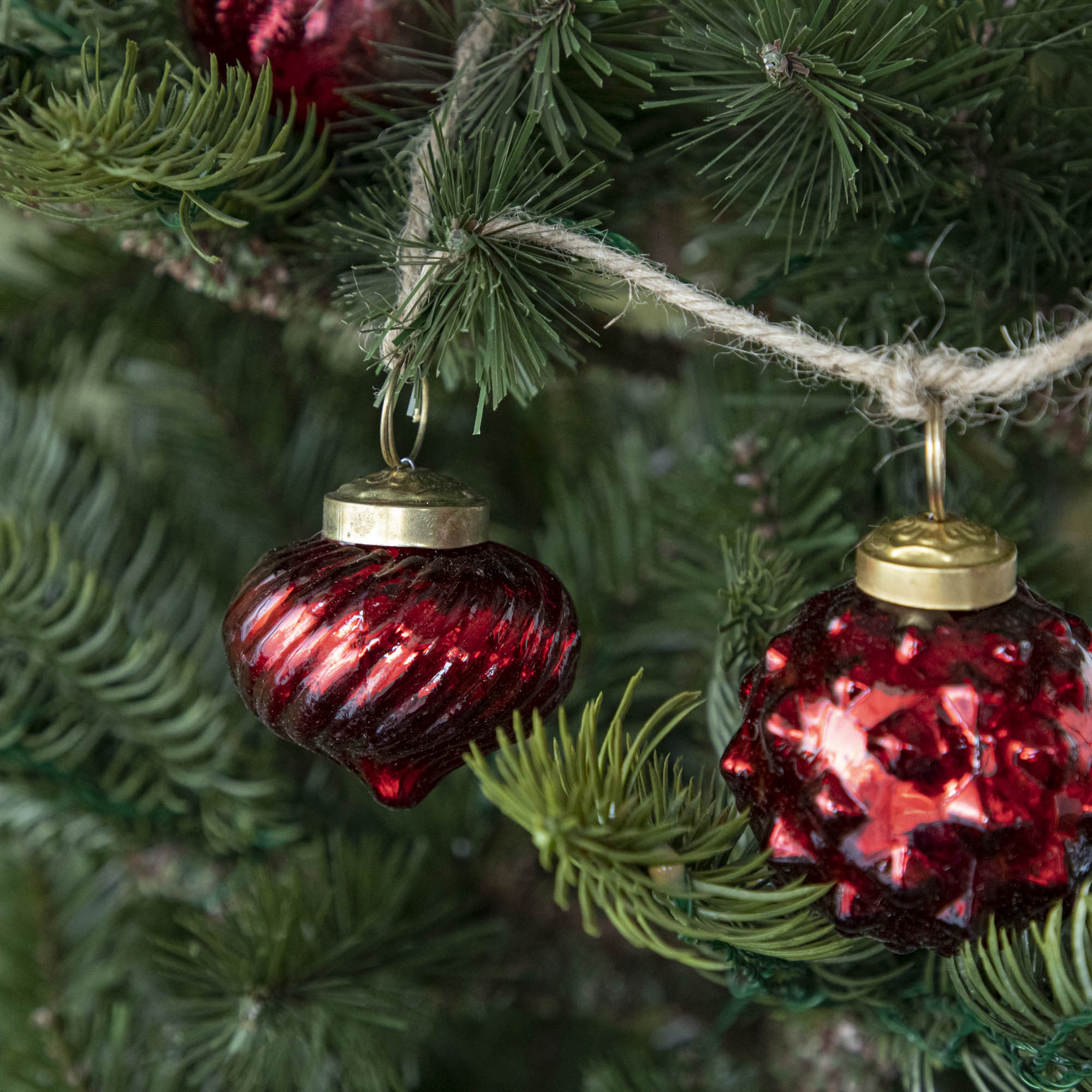 A close up of two Embossed Red Mercury Glass Ornaments showing the ribbed and spiked detailing and jute cord hanging on a tree.