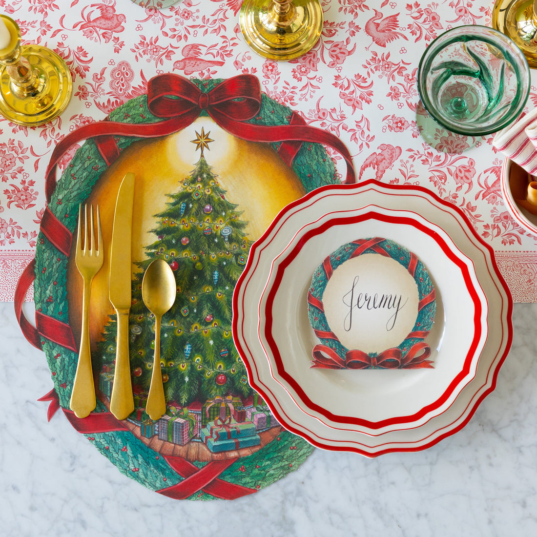 Christmas-themed table setting with red icing on the cake plates, gold cutlery, and candles on the O Christmas Tree Placemat and Red Regal Peacock Runner.