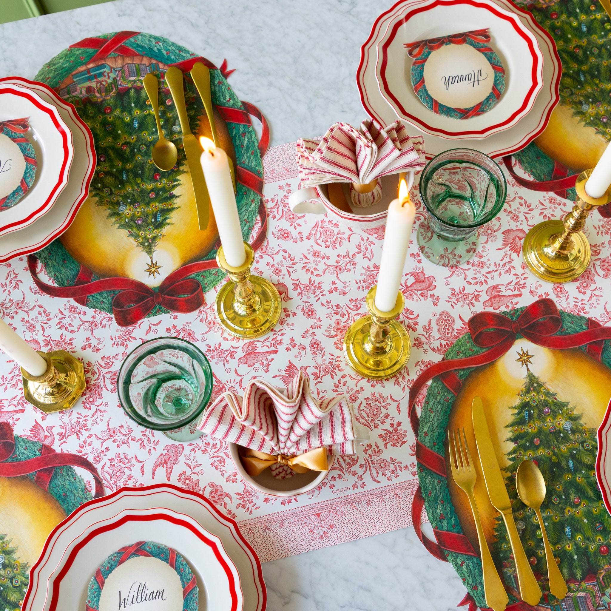 Decorative Christmas table setting with Red Icing on the Cake plates, O Christmas Tree Wreath Placemat, gold cutlery, and candles on the Red Regal Peacock Runner.