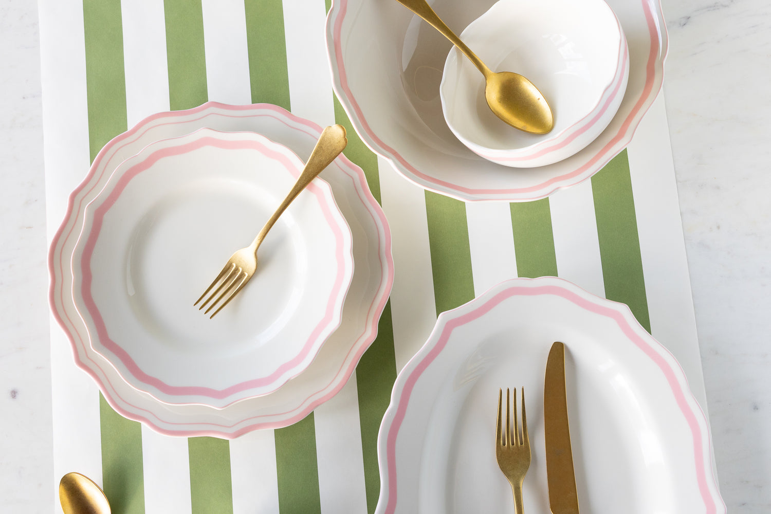 White plates and bowls with pink rims and gold cutlery on a striped runner.
