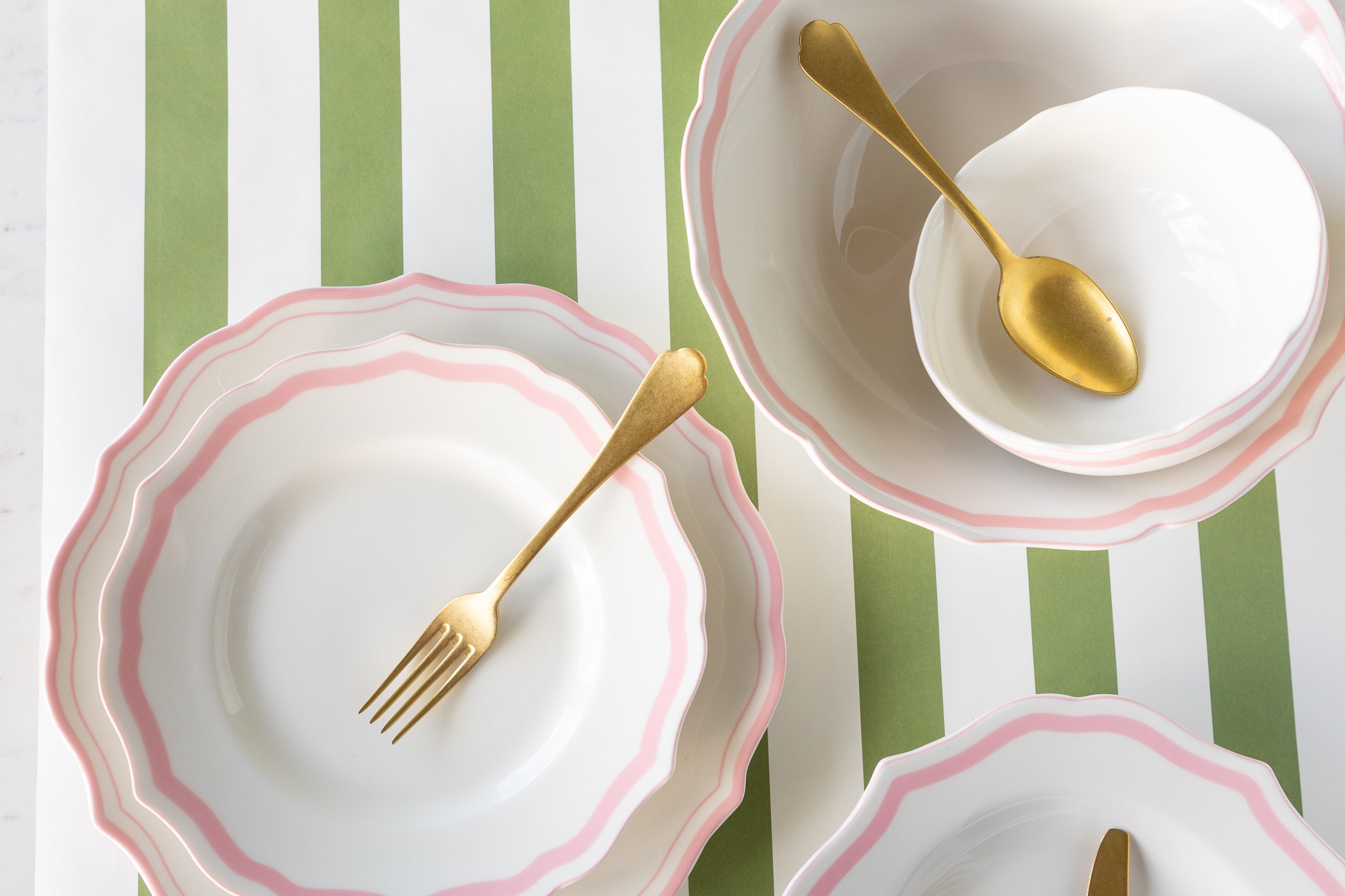 White plates with pink rims and gold cutlery on a green and white striped background.