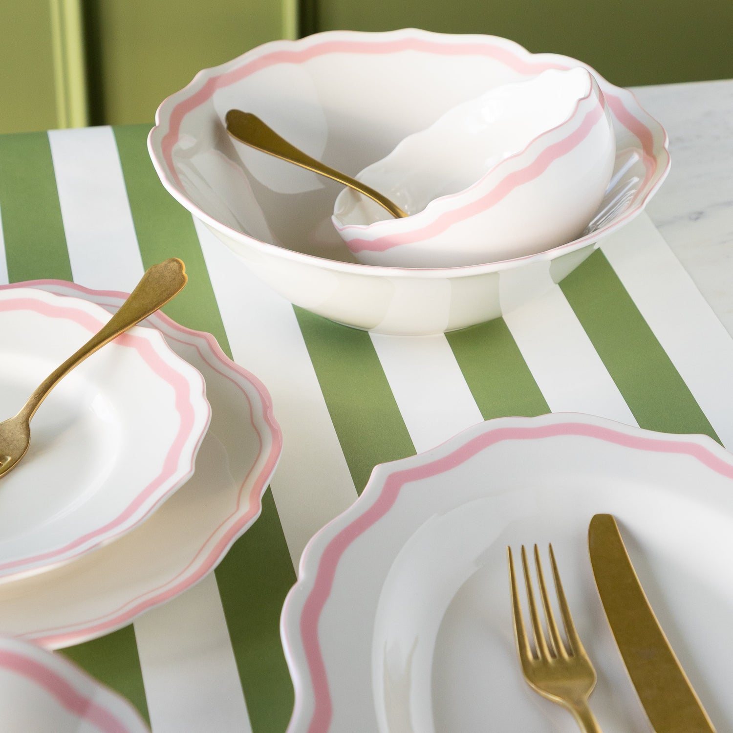 White plates and bowls with pink rims and gold cutlery on a striped runner.
