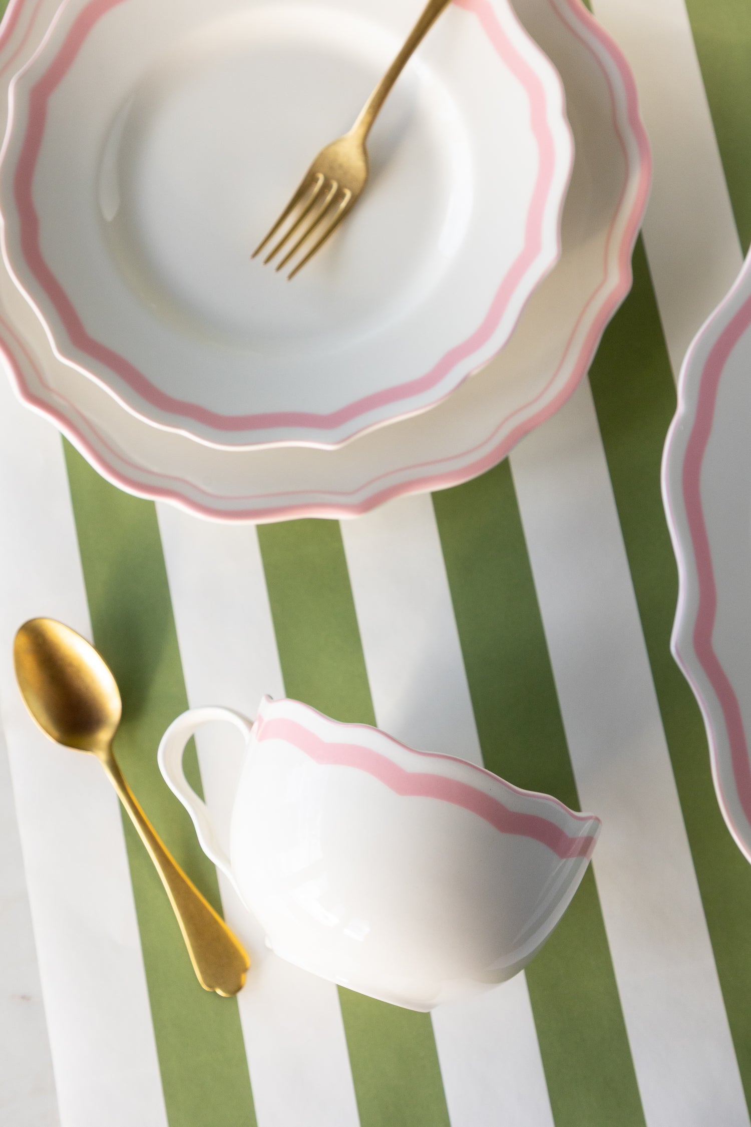 White plates and a mug with pink rims and gold cutlery on a striped runner.