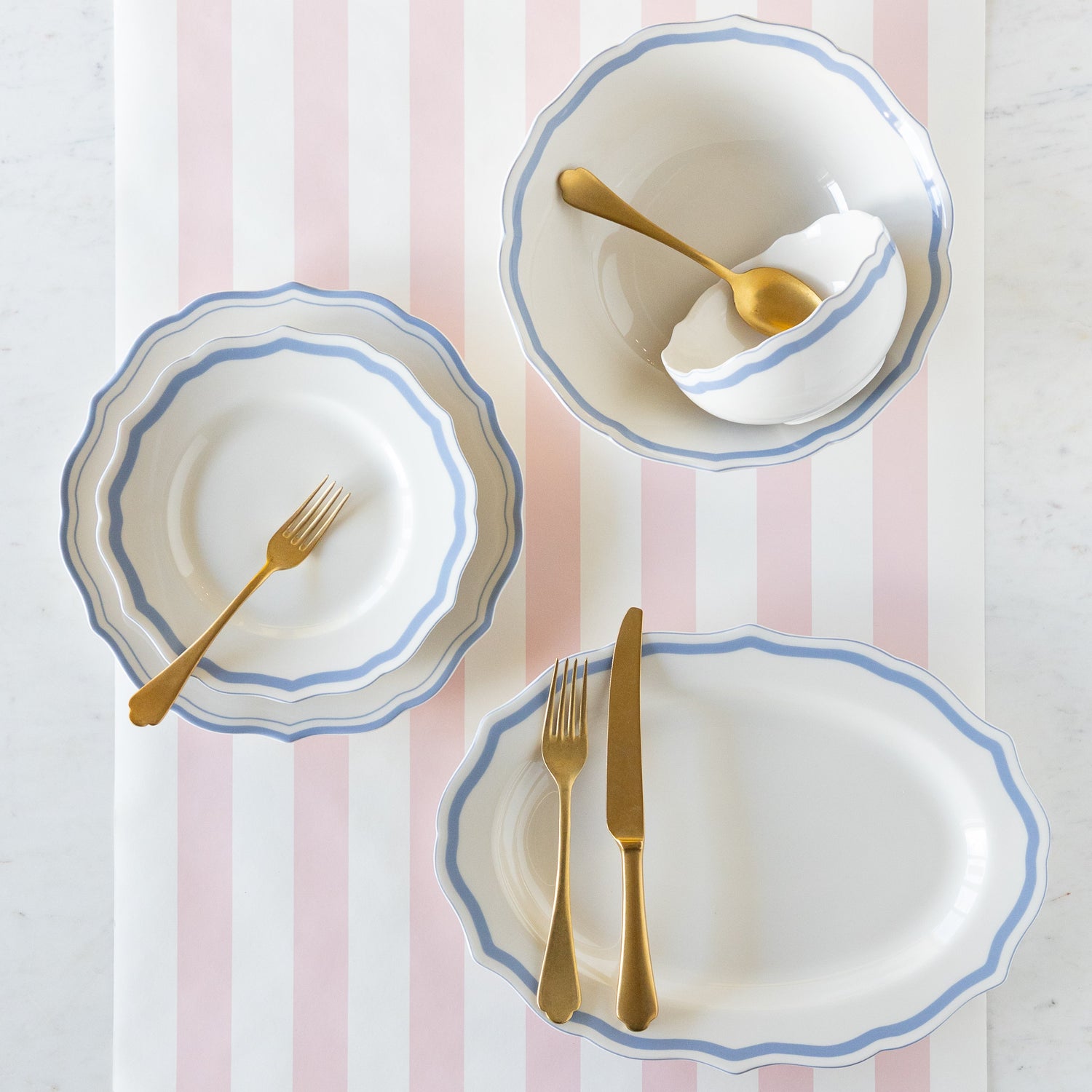 Set of ceramic dinnerware with blue rims and gold cutlery on the Pink Classic Stripe Runner.