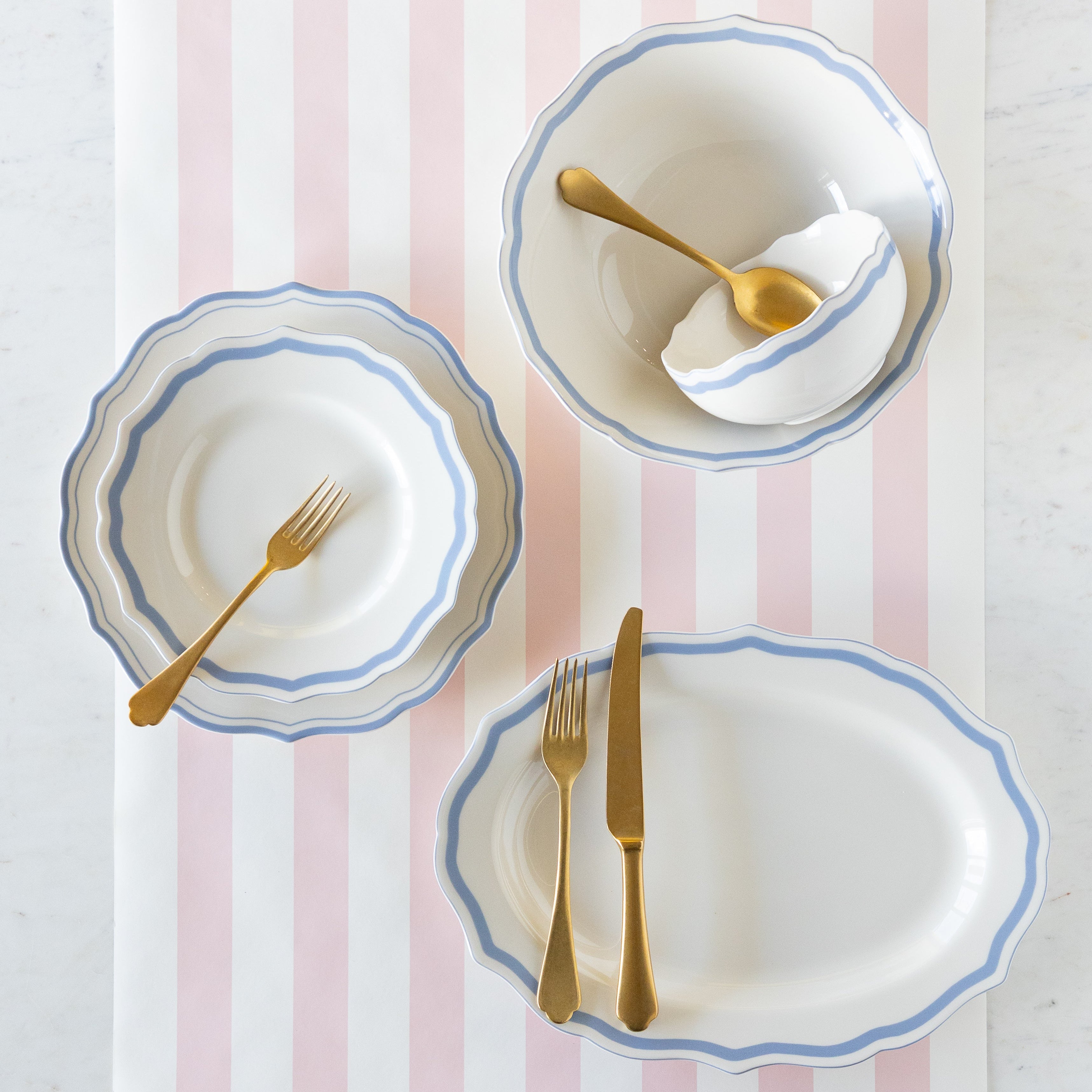 Set of ceramic dinnerware with blue rims and gold cutlery on the Pink Classic Stripe Runner.