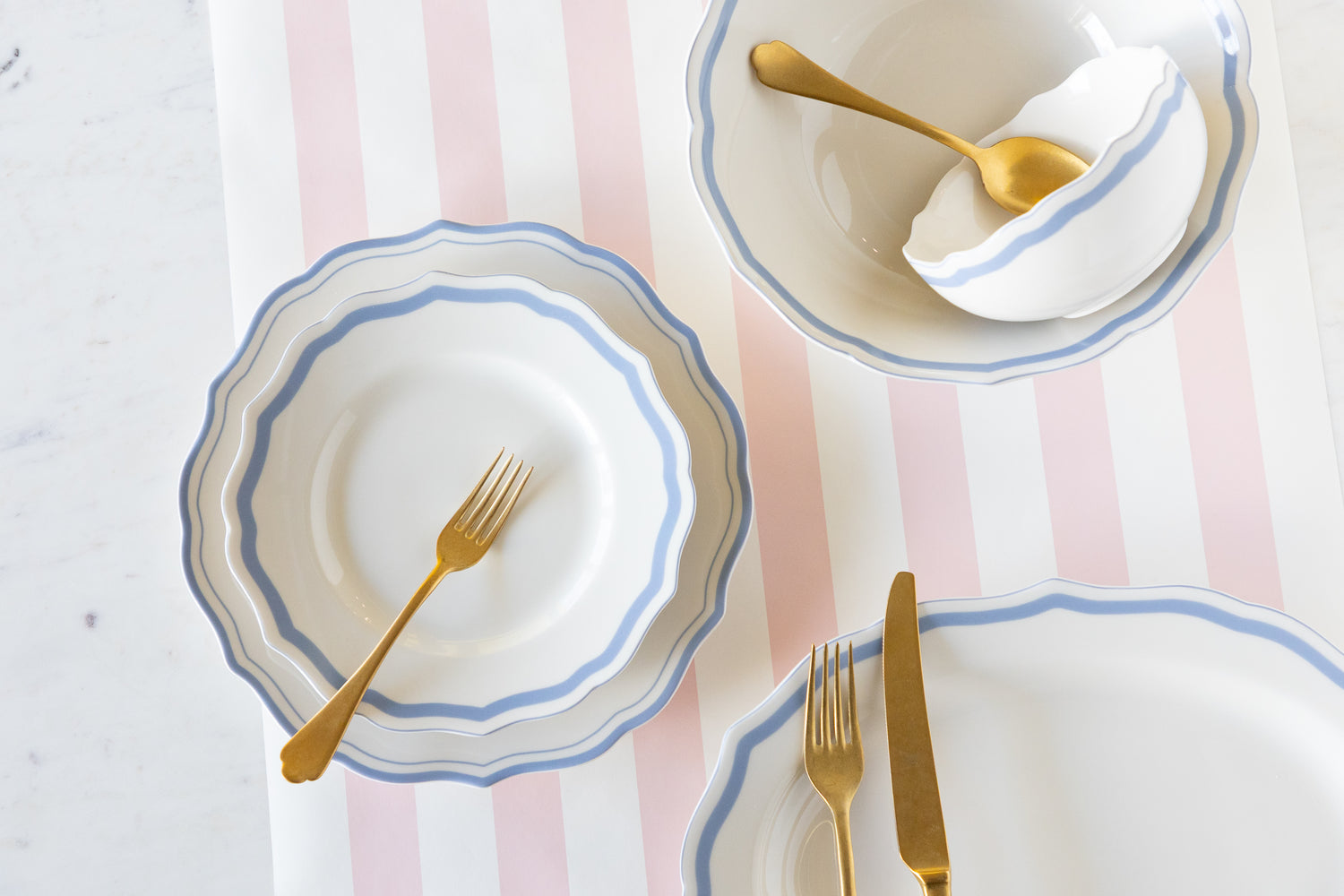 Dinnerware set with plates, cutlery, and a striped tablecloth on a light background.