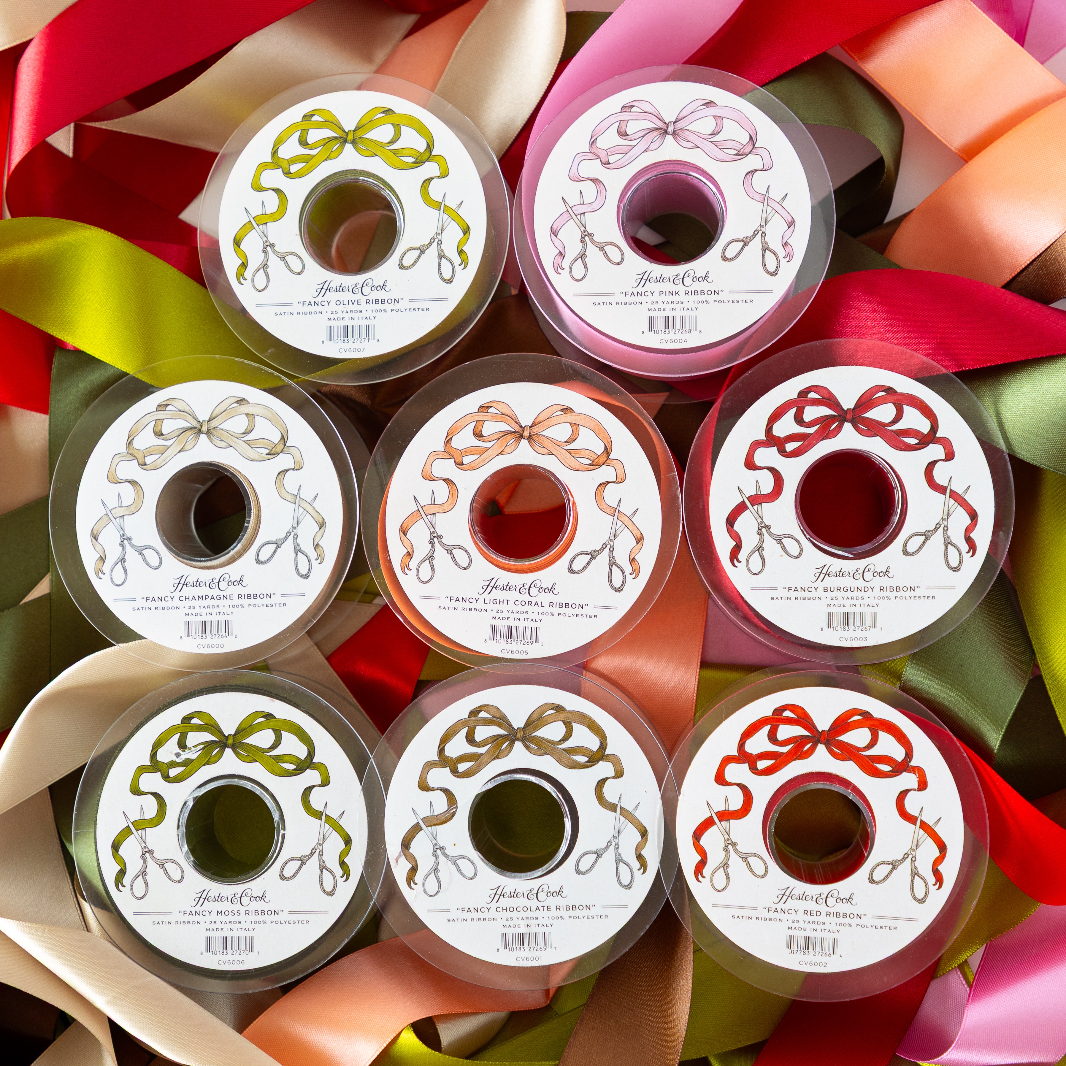 Assorted spools of Hester &amp; Cook Fancy Ribbon with decorative labels on top of colorful ribbons.