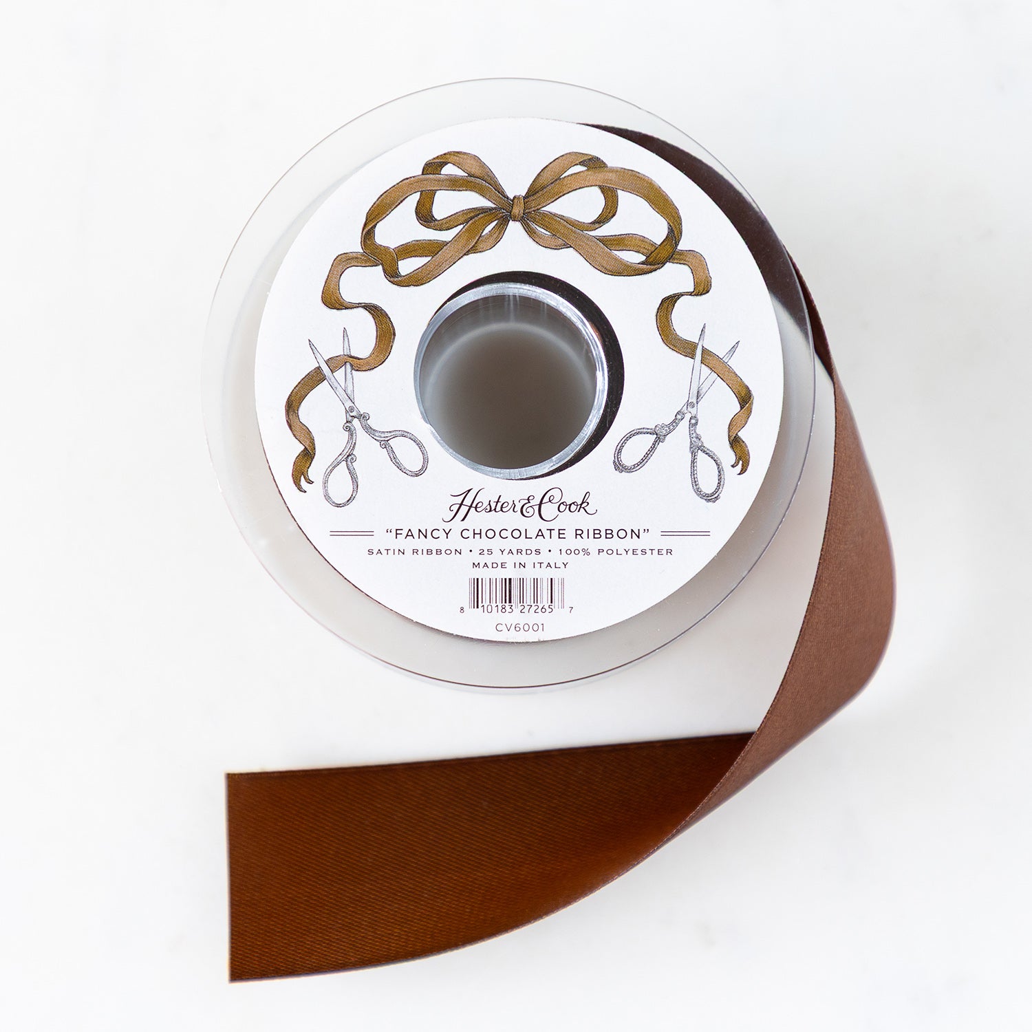 A spool of chocolate-brown satin ribbon with a label featuring illustrated scissors and brown bow branded "Hester &amp; Cook Fancy Chocolate Ribbon.