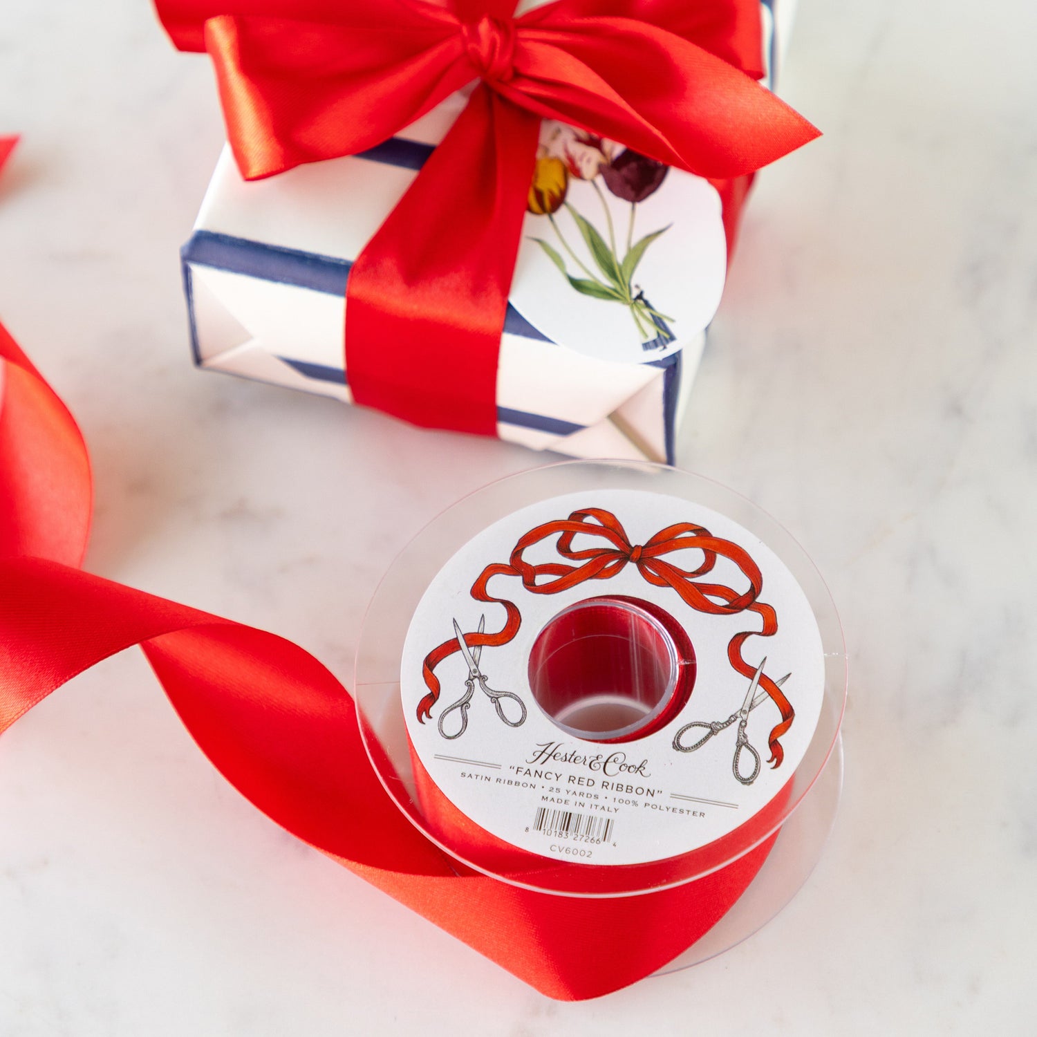 Spool of  Fancy Red Ribbon with a decorative label next to a wrapped gift with a red ribbon bow.