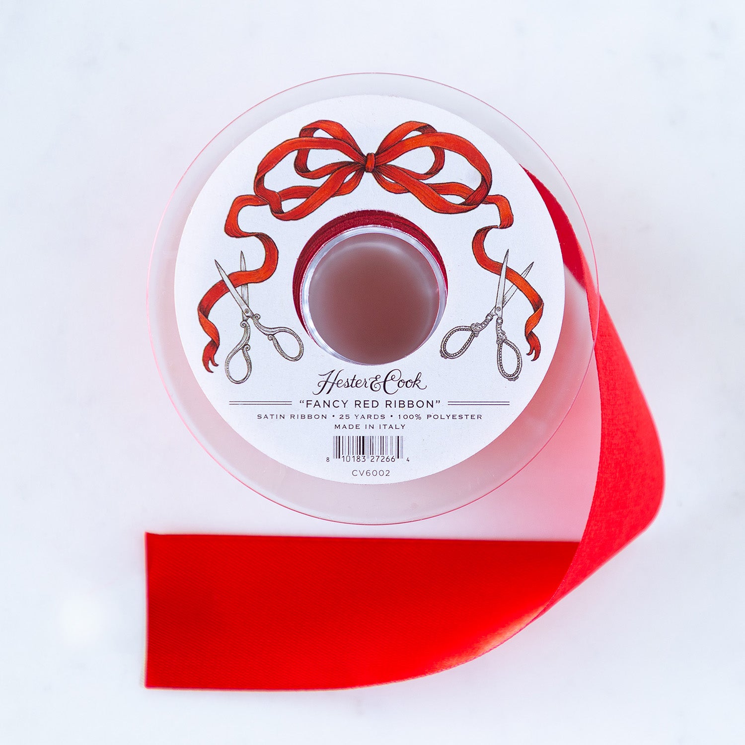 A spool of red satin ribbon with a label featuring illustrated scissors and red bow branded &quot;Hester &amp; Cook Fancy Red Ribbon.