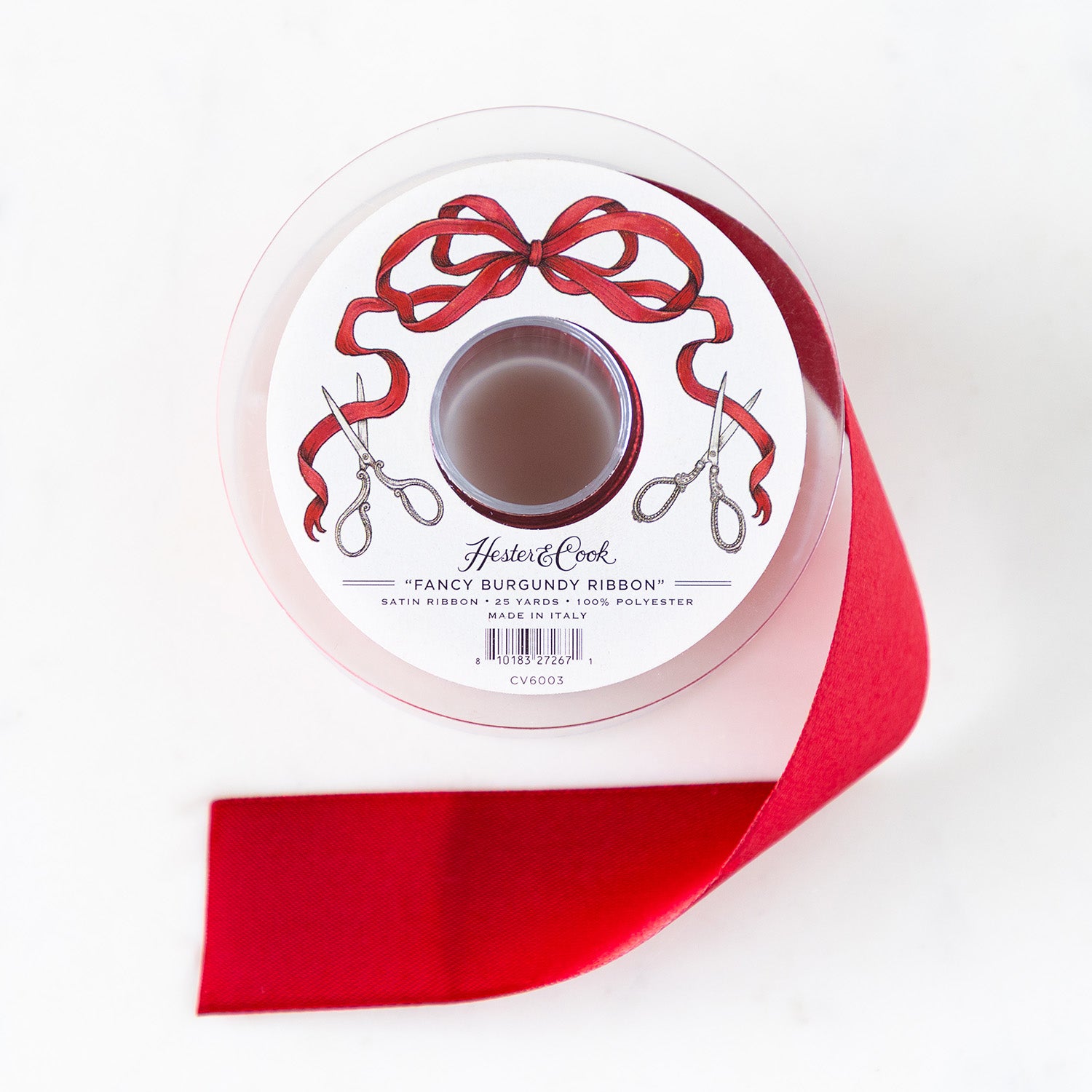 A spool of burgundy satin ribbon with a label featuring illustrated scissors and a red bow, branded &quot;Hester &amp; Cook Fancy Olive Ribbon.