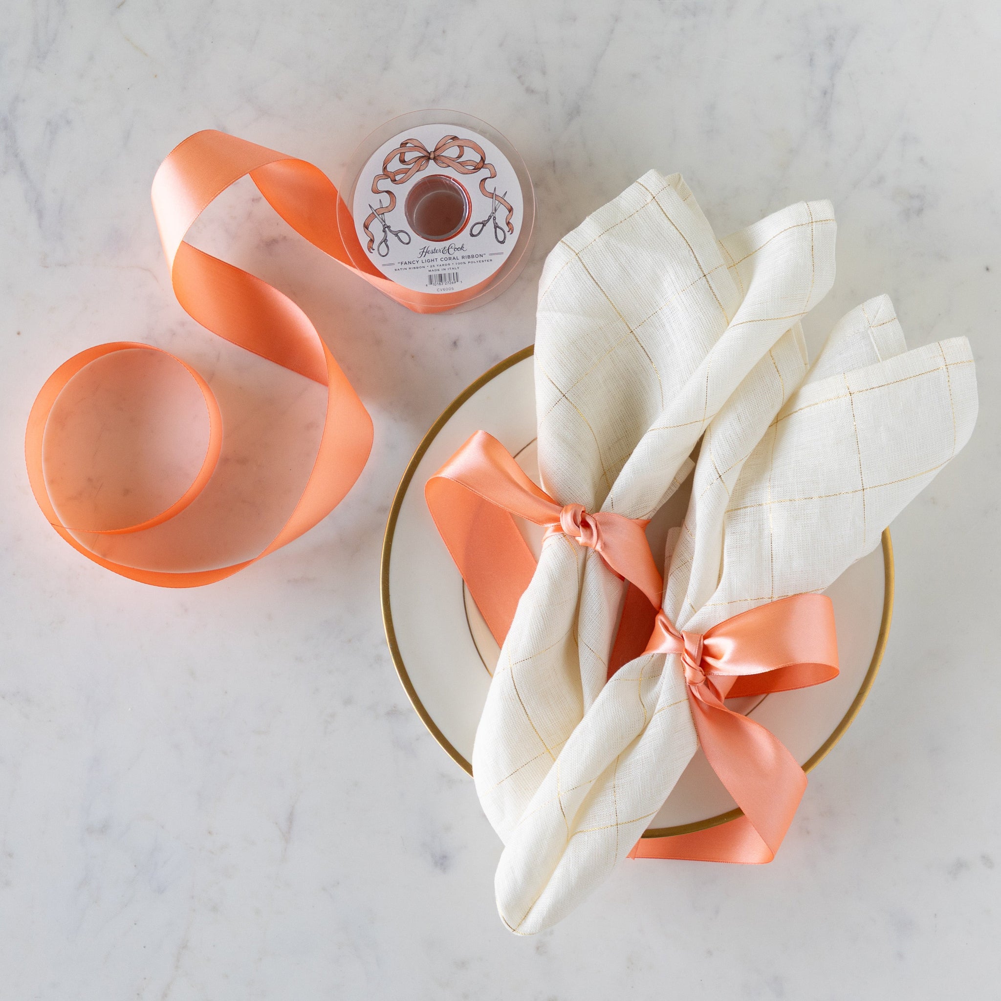 Elegant napkins tied together with the Fancy Light Coral Ribbon, next to a spool of the Fancy Light Coral Ribbon.