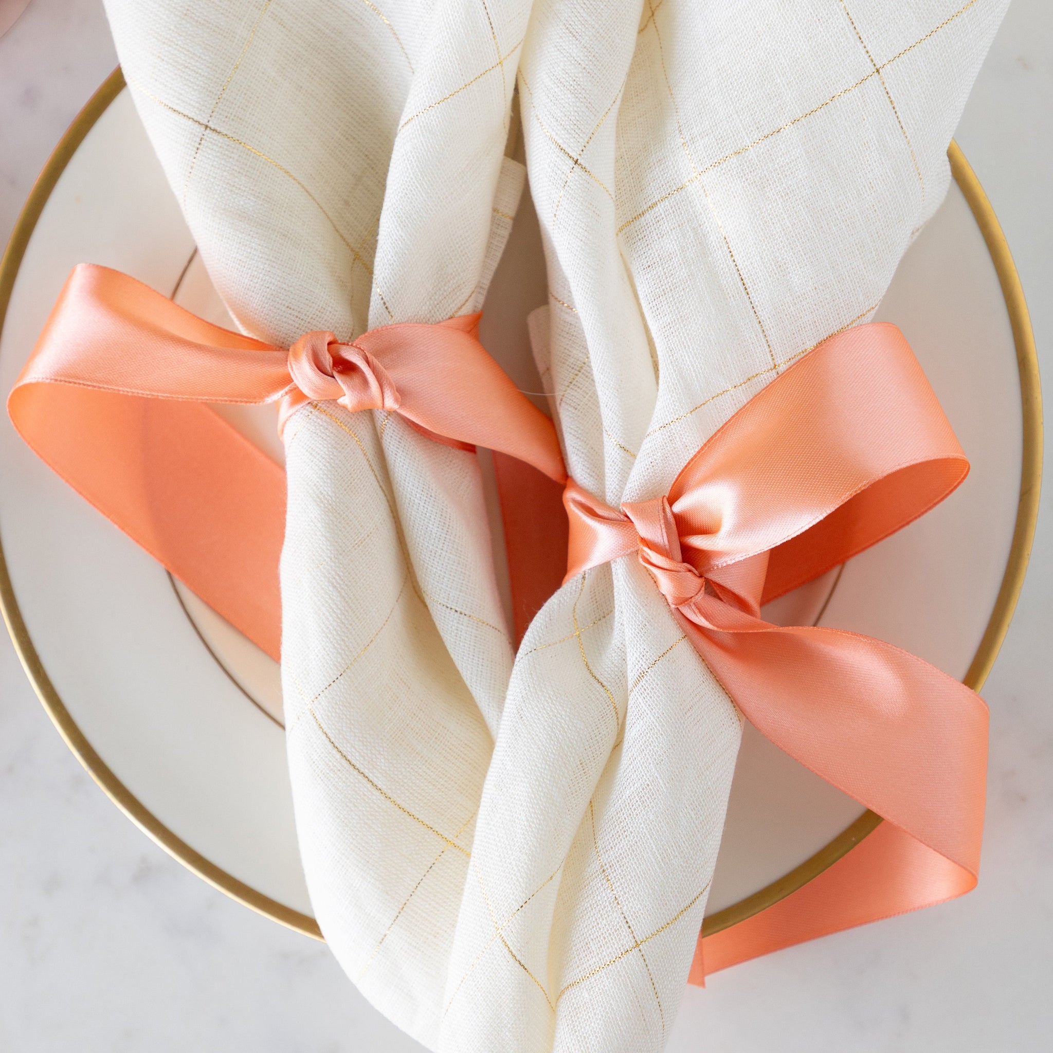 Two elegant napkins tied with the Fancy Light Coral Ribbon on a gold rimmed plate.