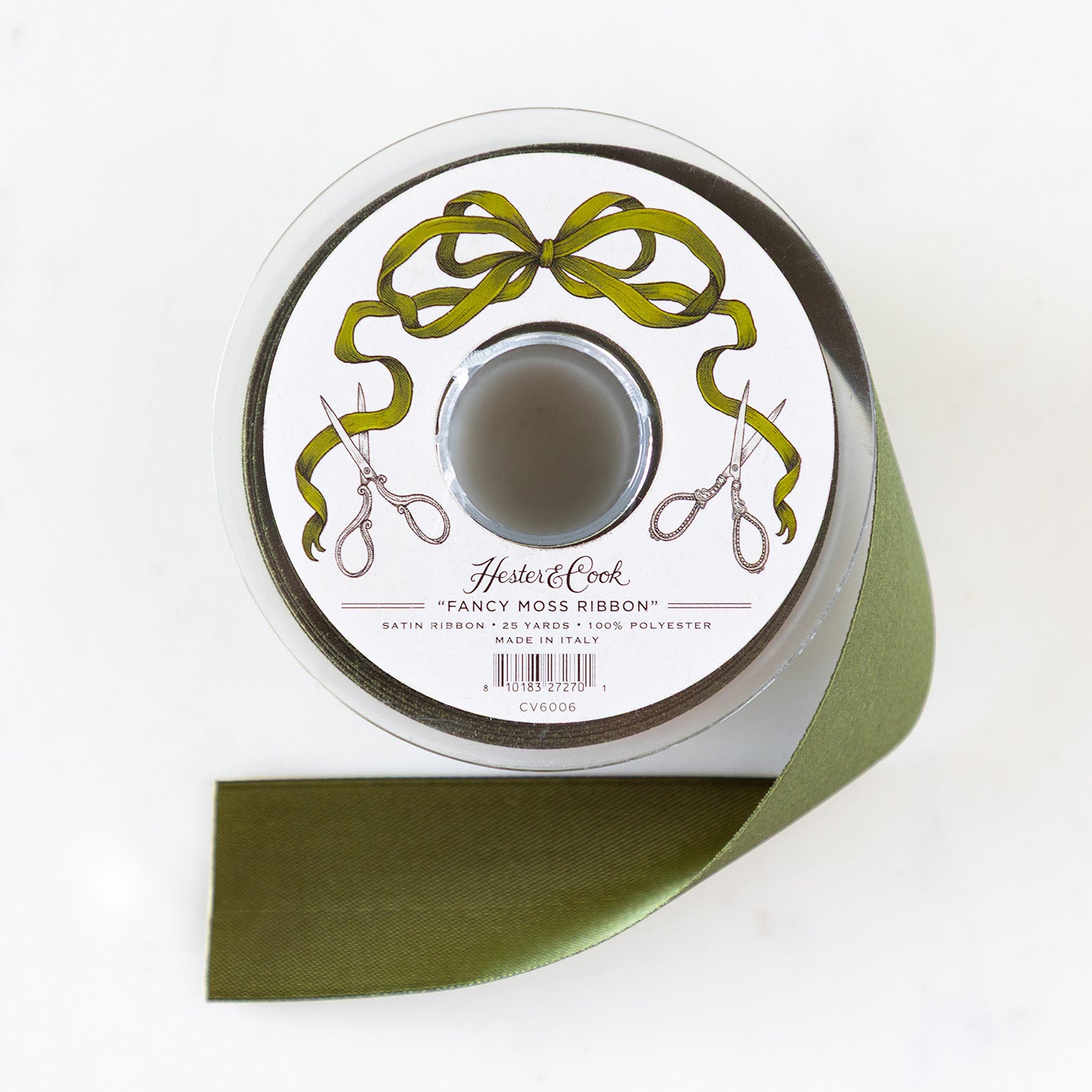 A spool of moss-green satin ribbon with a label featuring illustrated scissors and moss bow, branded "Hester &amp; Cook Fancy Moss Ribbon.