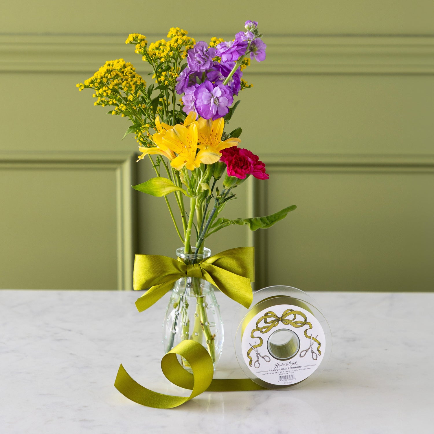 Vase of colorful flowers with a green ribbon bow tied around it, next to a spool of Fancy Olive Ribbon.