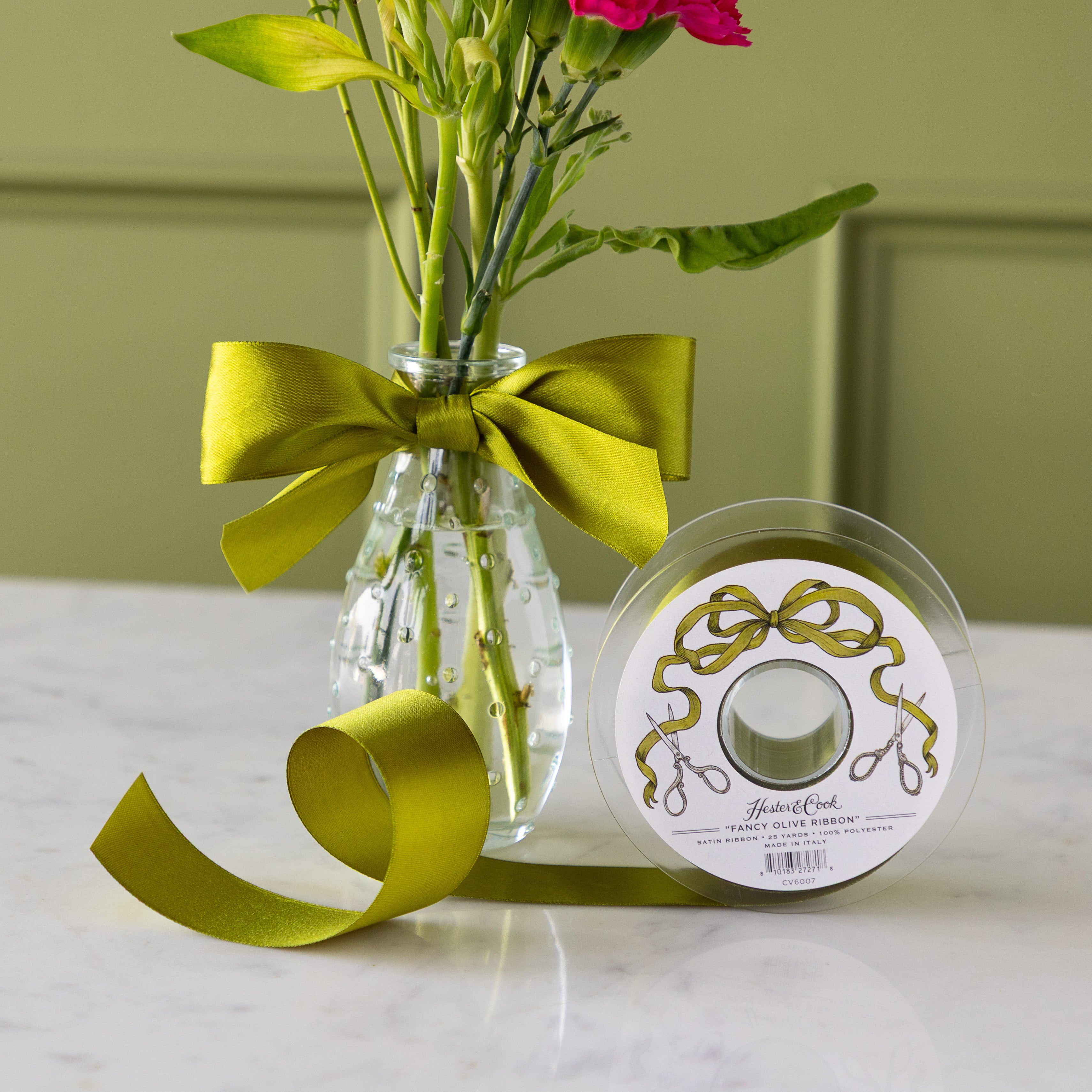Vase of colorful flowers with a green ribbon bow tied around it, next to a spool of Fancy Olive Ribbon.