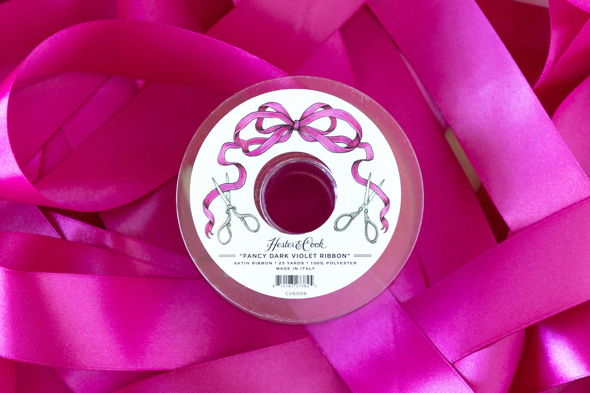 Spool of dark violet ribbon with a decorative label on a background of dark violet ribbons.