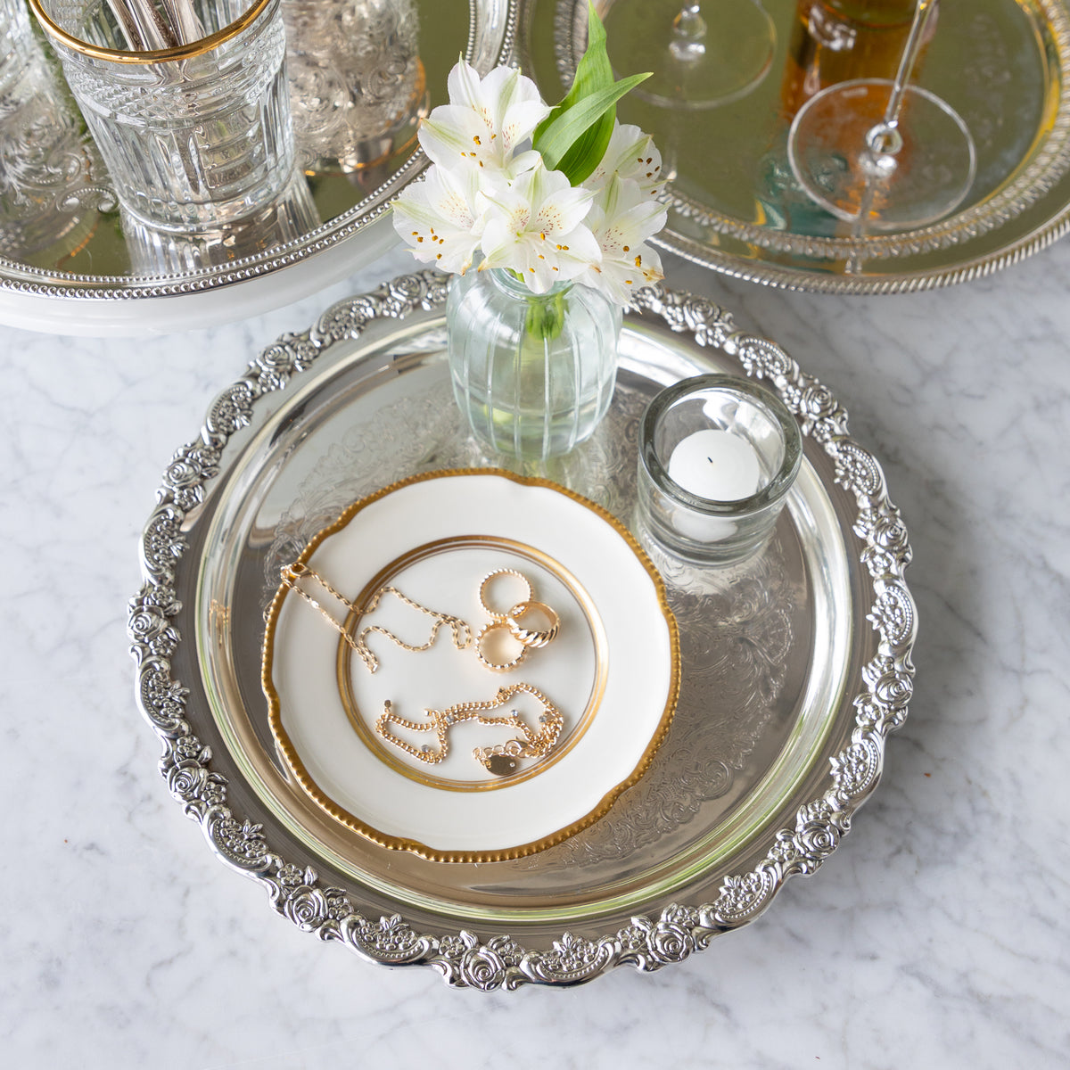 Silver tray with jewelry, white plate, and small candle on a marble surface.