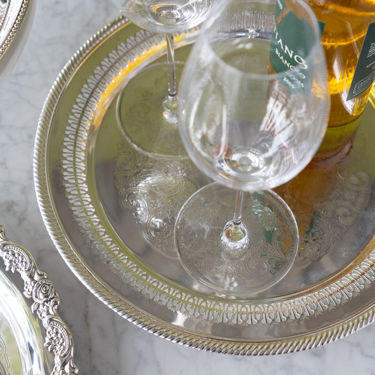 Wine glasses on a decorative silver tray with a bottle of wine in the background.