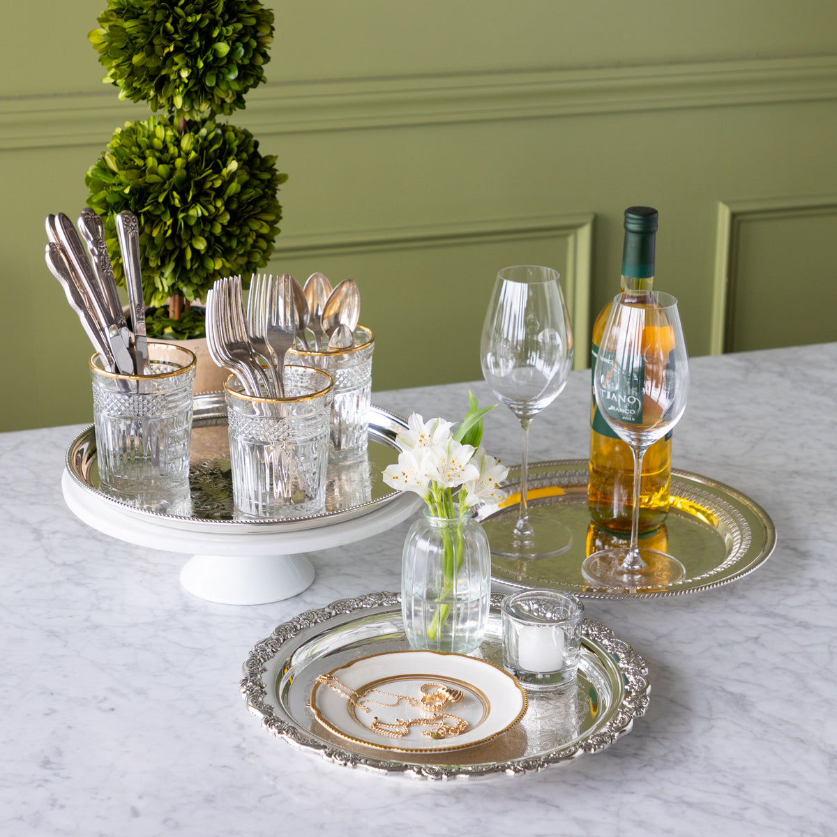 Dining table setting with cutlery, glasses, and a bottle of wine against a green wall.