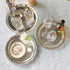 Decorative silver trays with jewelry, glasses, and a bottle on a marble surface.