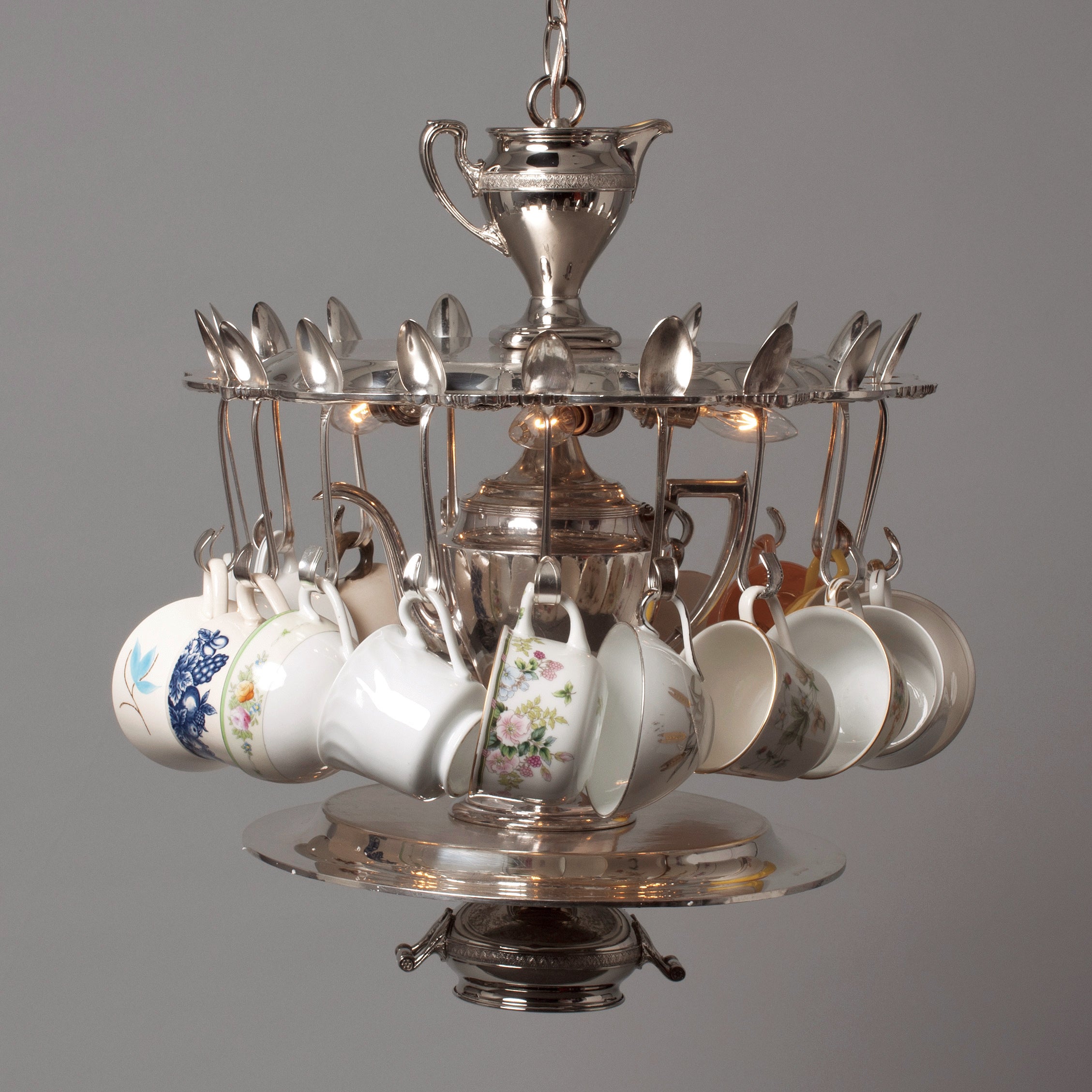 A whimsical chandelier crafted using a vintage silver-plate teapot, sugar/creamers, serving trays and teaspoons, and topped off with assorted vintage teacups.
