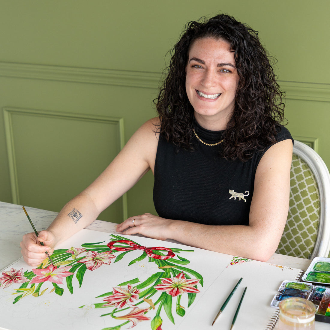 Christie Vergona painting a the Die-cut Amaryllis Placemat on paper with a green wall in the background.
