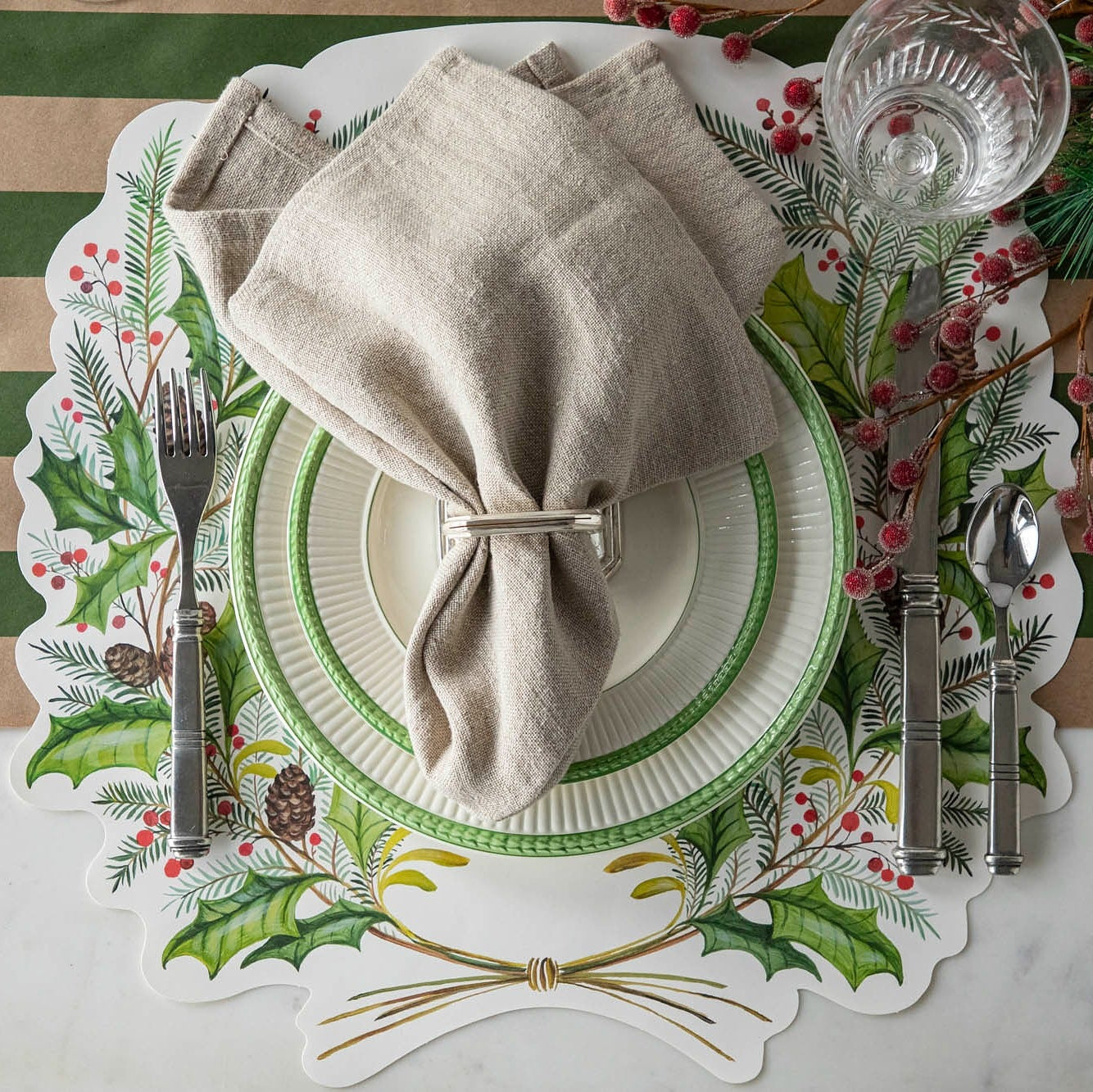 Christmas-themed place setting featuring the Die-cut Christmas Sprigs Placemat, decorative napkin, and green rimmed dinner plates on the Kraft Green Classic Stripe Runner.