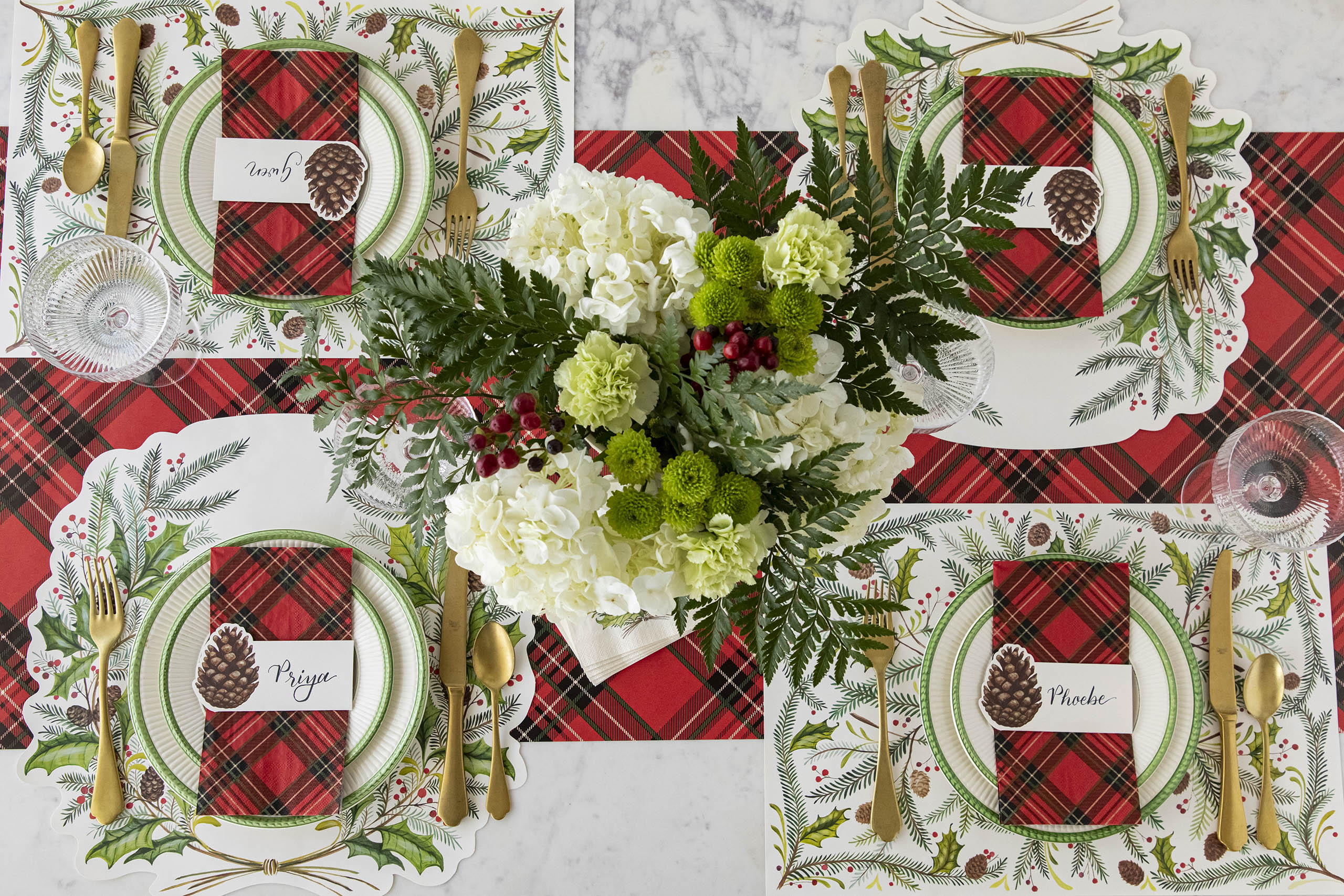 A woodland themed table setting featuring Die-cut Christmas Sprigs and Christmas Sprigs Placemats, Pinecone Place Cards, Red Plaid Guest Napkins and a floral centerpiece on the Red Plaid Runner.