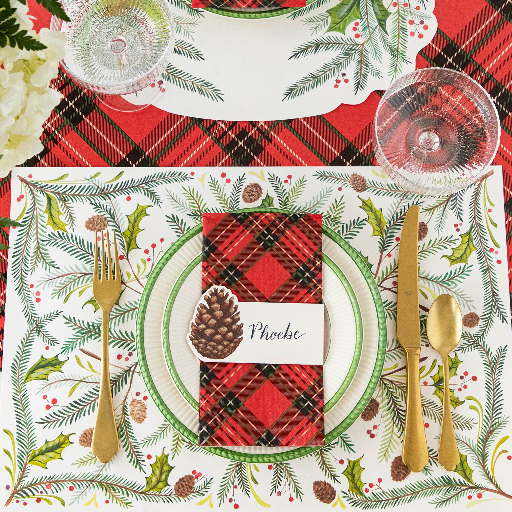 Christmas-themed table setting with the Christmas Sprigs Placemat, Pinecone Place Card, Red Plaid Napkin and gold flatware on the Red Plaid Runner.