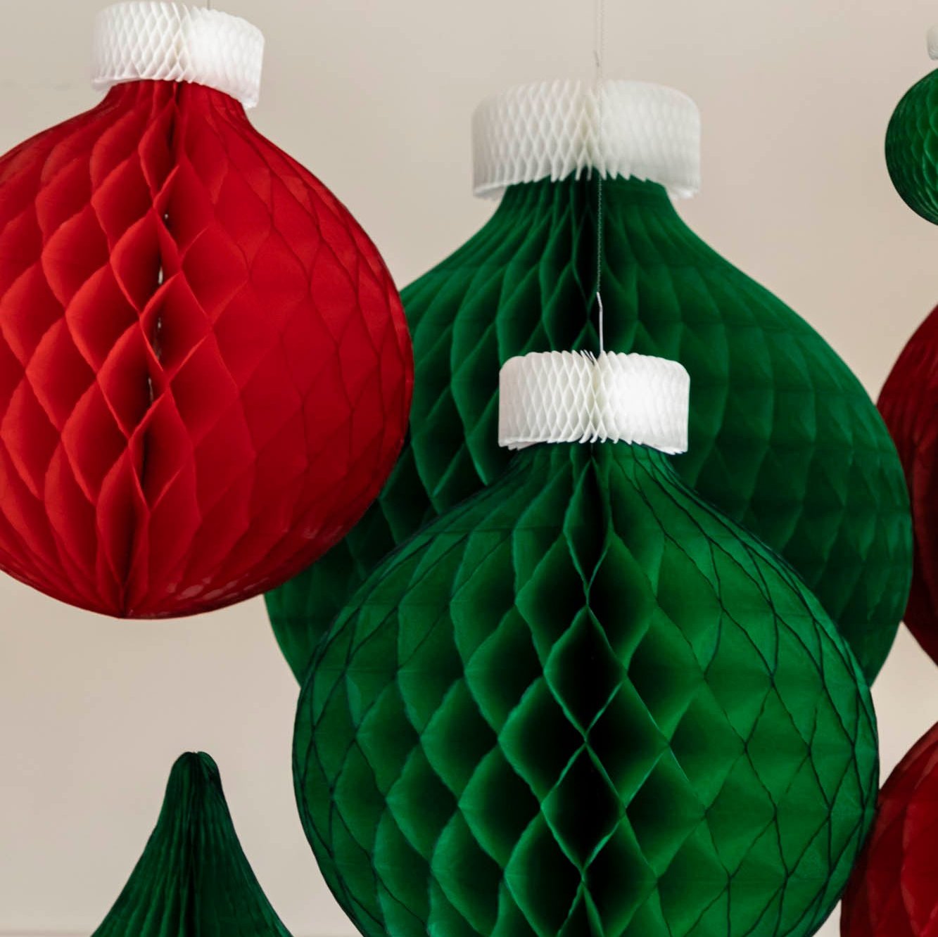 Green and red Honeycomb Medium Classic Ornaments hanging from the ceiling amongst other honeycomb classic ornaments.