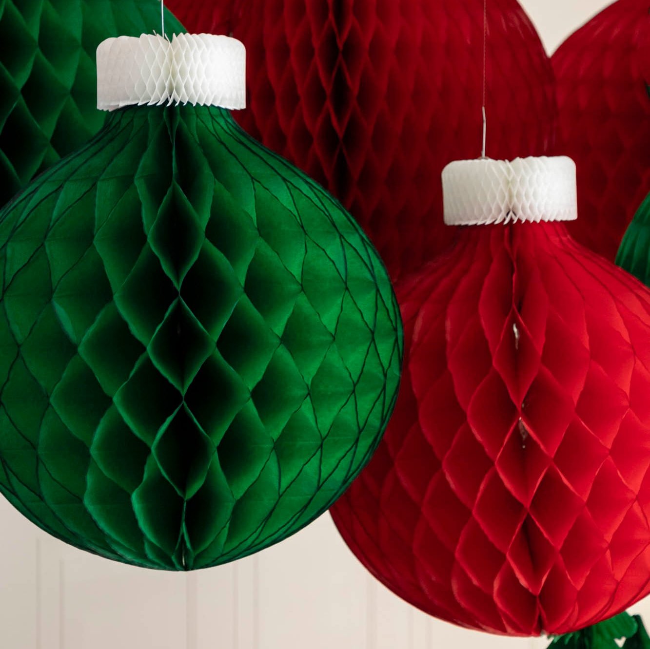 Green and red Honeycomb Medium Classic Ornaments hanging from the ceiling amongst other honeycomb classic ornaments.