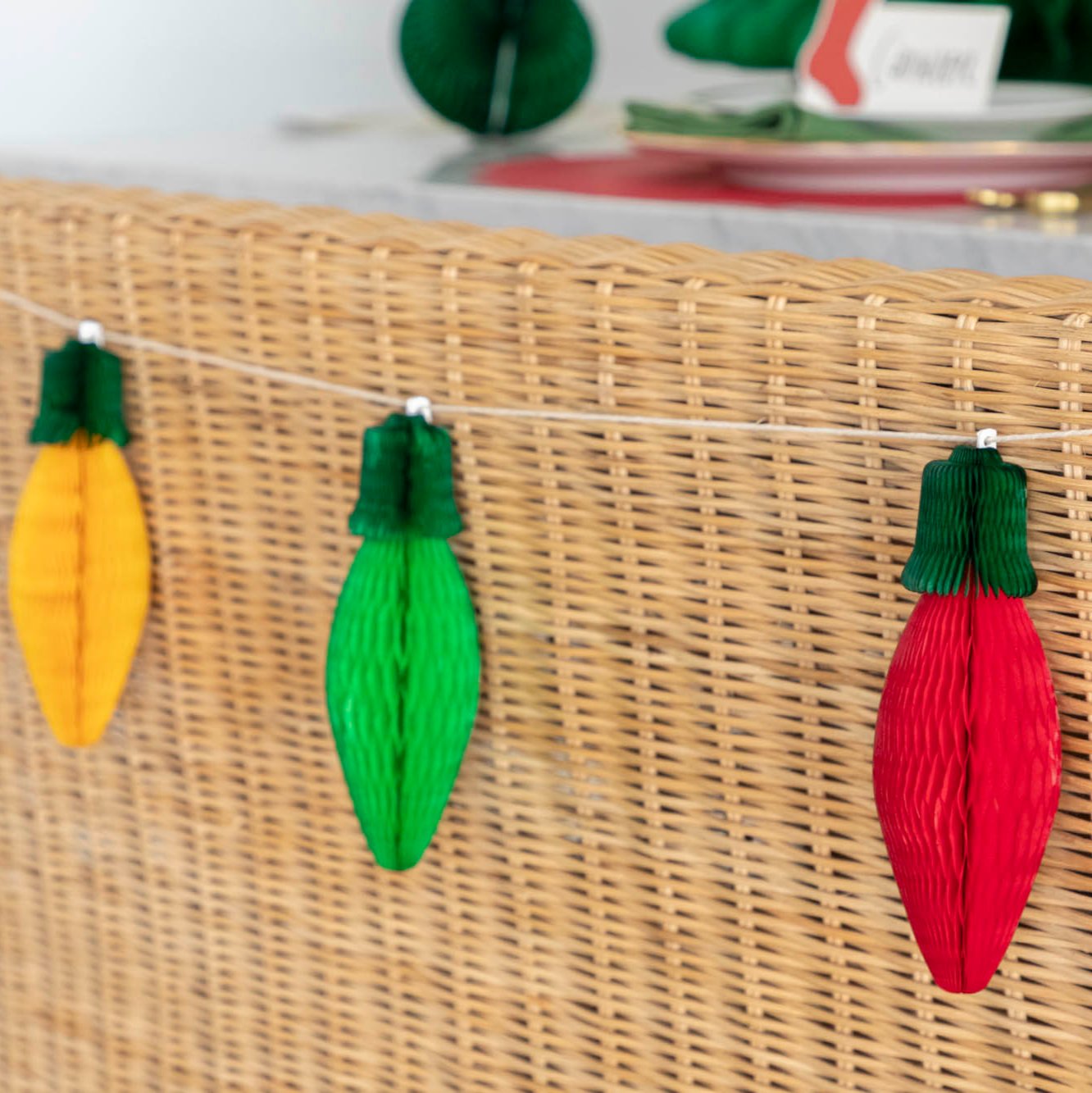 A close up of the the Honeycomb Christmas Lights with green tops and green, yellow and red bulbs, strung on the back of a wicker bench.