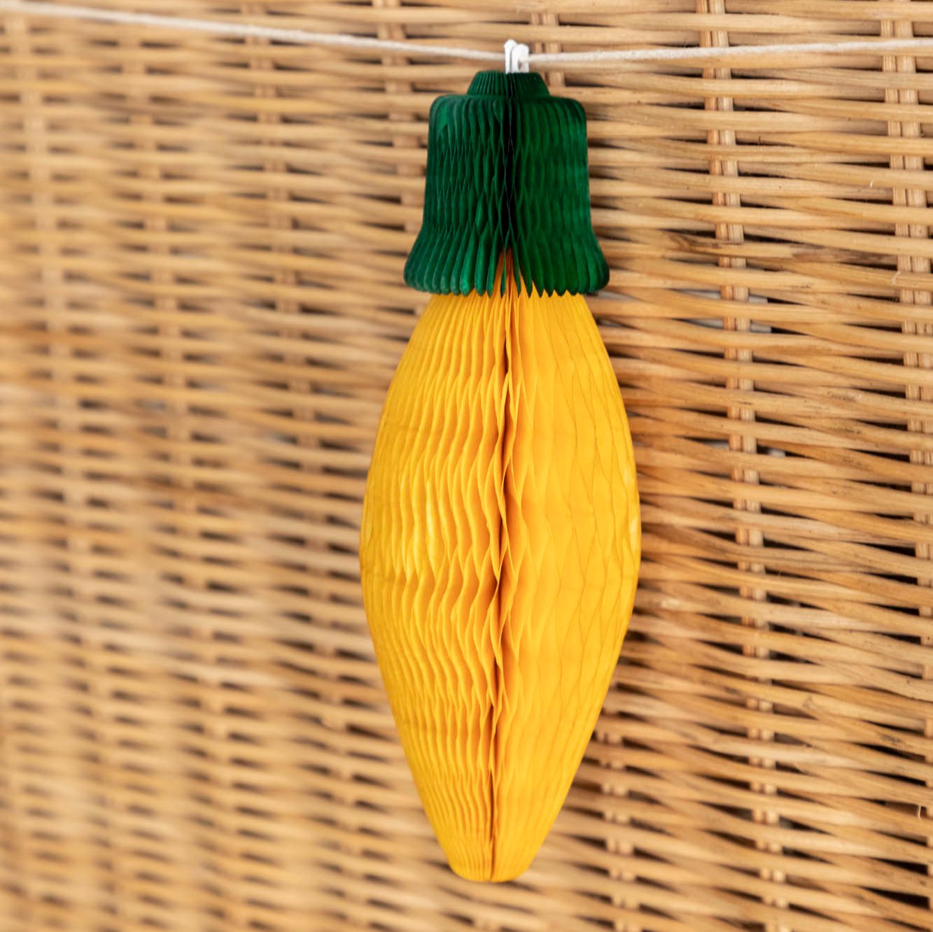 A close up of the the Honeycomb Christmas Light with a yellow bulb and green top, strung on the back of a wicker bench.