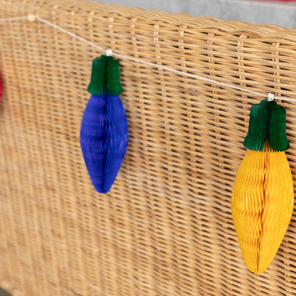 A close up of the the Honeycomb Christmas Lights with green tops and a blue or yellow bulb, strung on the back of a wicker bench.