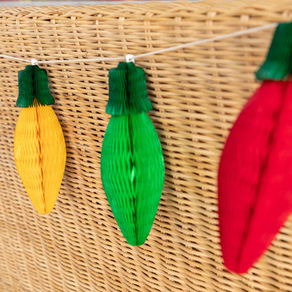 Green, red and yellow honeycomb Christmas Lights strung on the back of a wicker bench.