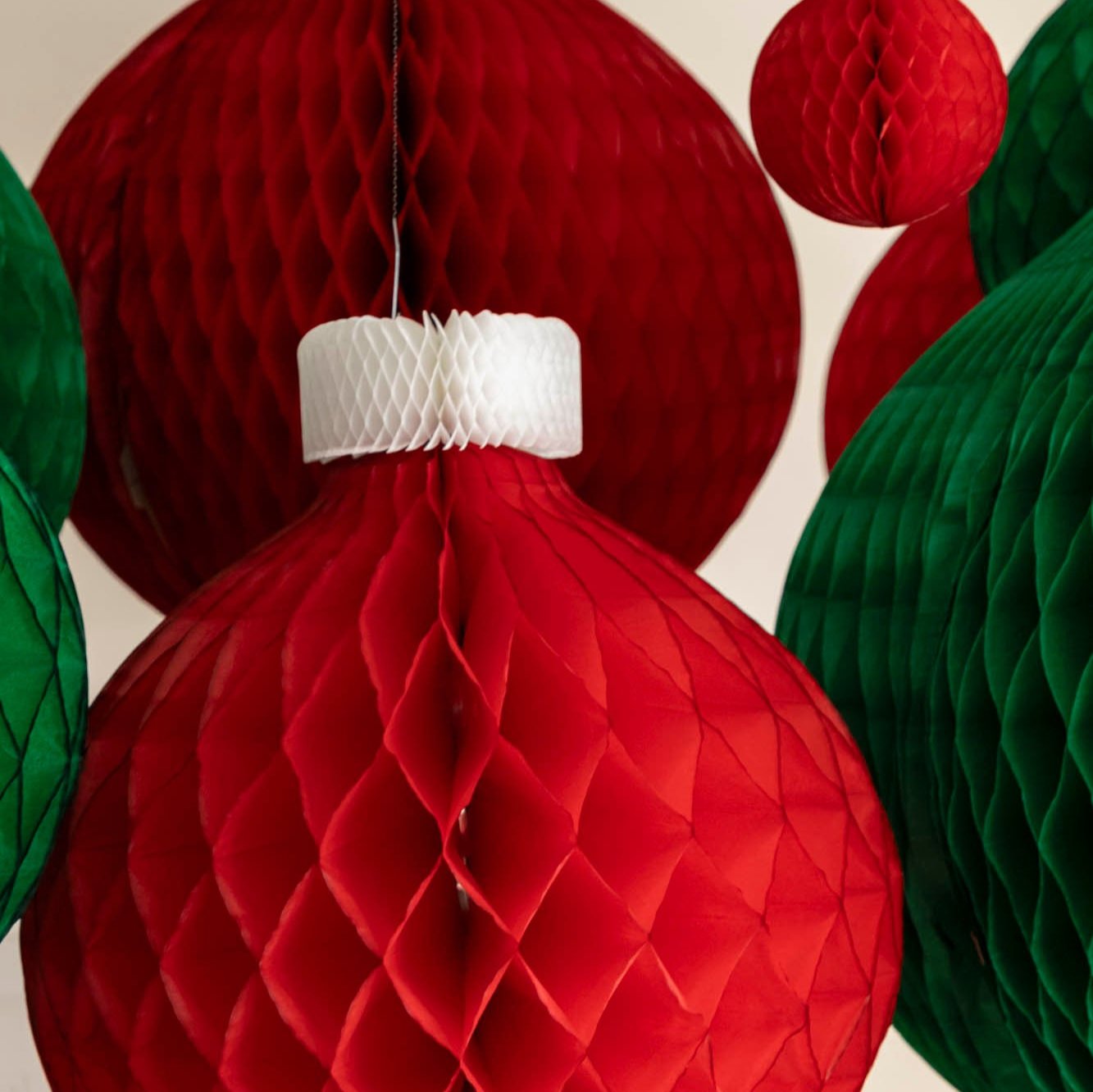 A close view of the red Honeycomb Classic Ornament showing its red base and white top, hanging amongst various sized honeycomb classic ornaments.