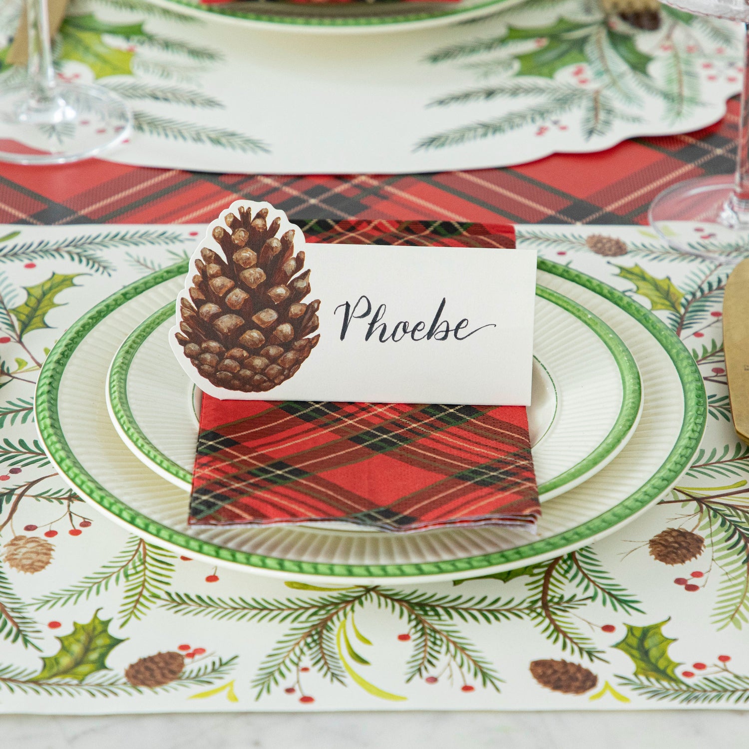 Christmas-themed place setting with the Pine Cone Place Card, Red Plaid Guest Napkin, Christmas Sprigs Placemat and Red Plaid Runner.