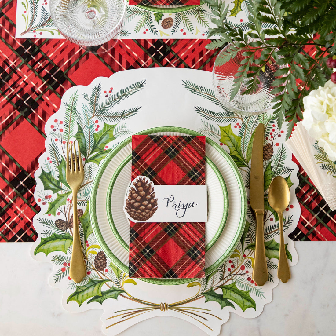 Christmas-themed table setting with the Die-cut Christmas Sprigs Placemat, Red Plaid Napkin, Pinecone Place Card and gold cutlery on the Red Plaid Runner.