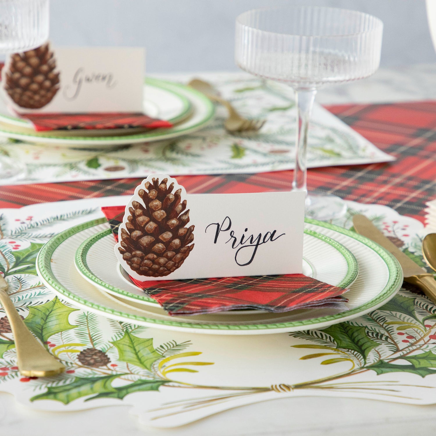 The Pinecone Place Card atop a place setting with the Die-cut Christmas Sprigs, Red Plaid Guest Napkin and Red Plaid Runner underneath.