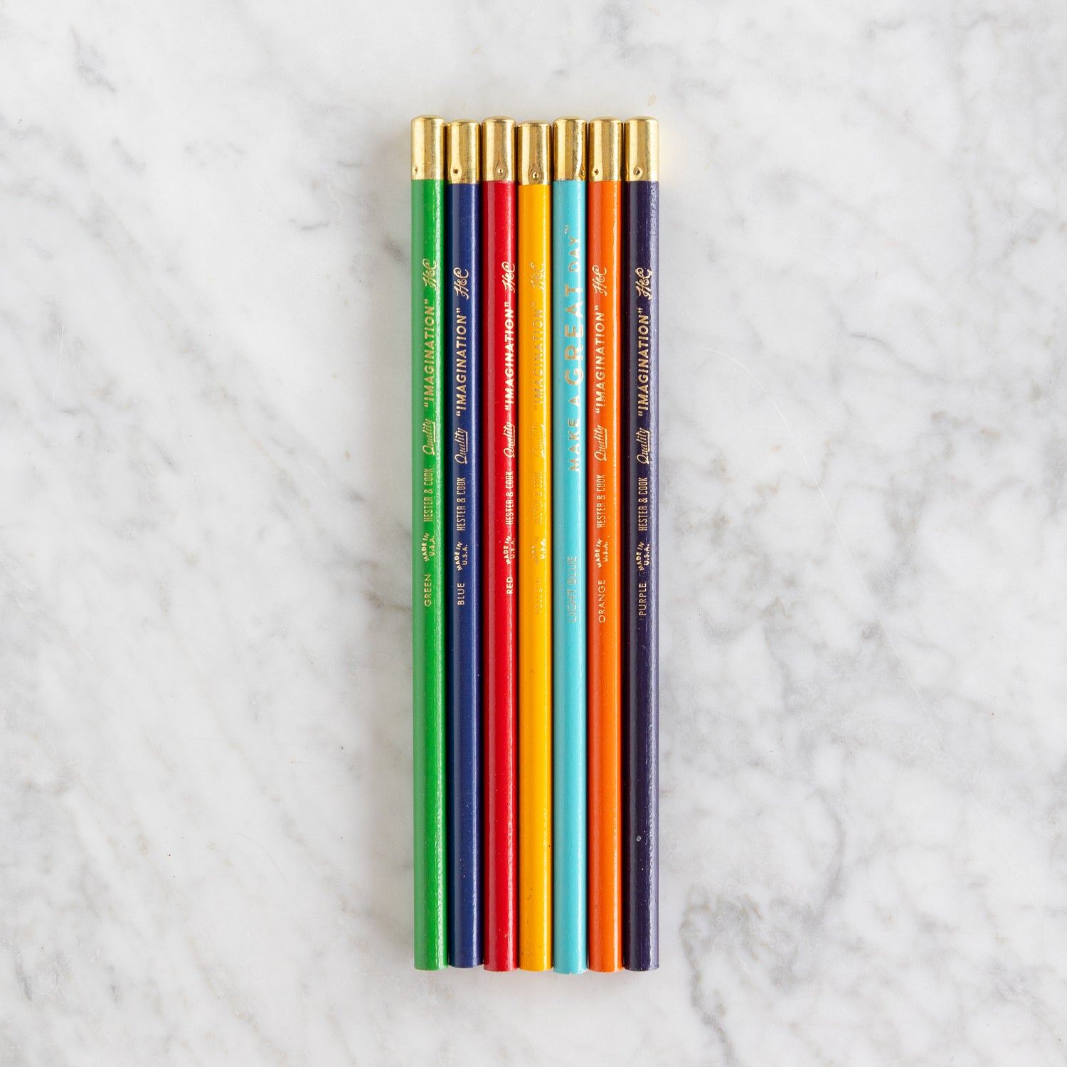 Set of colored pencils with gold caps on a marble surface.