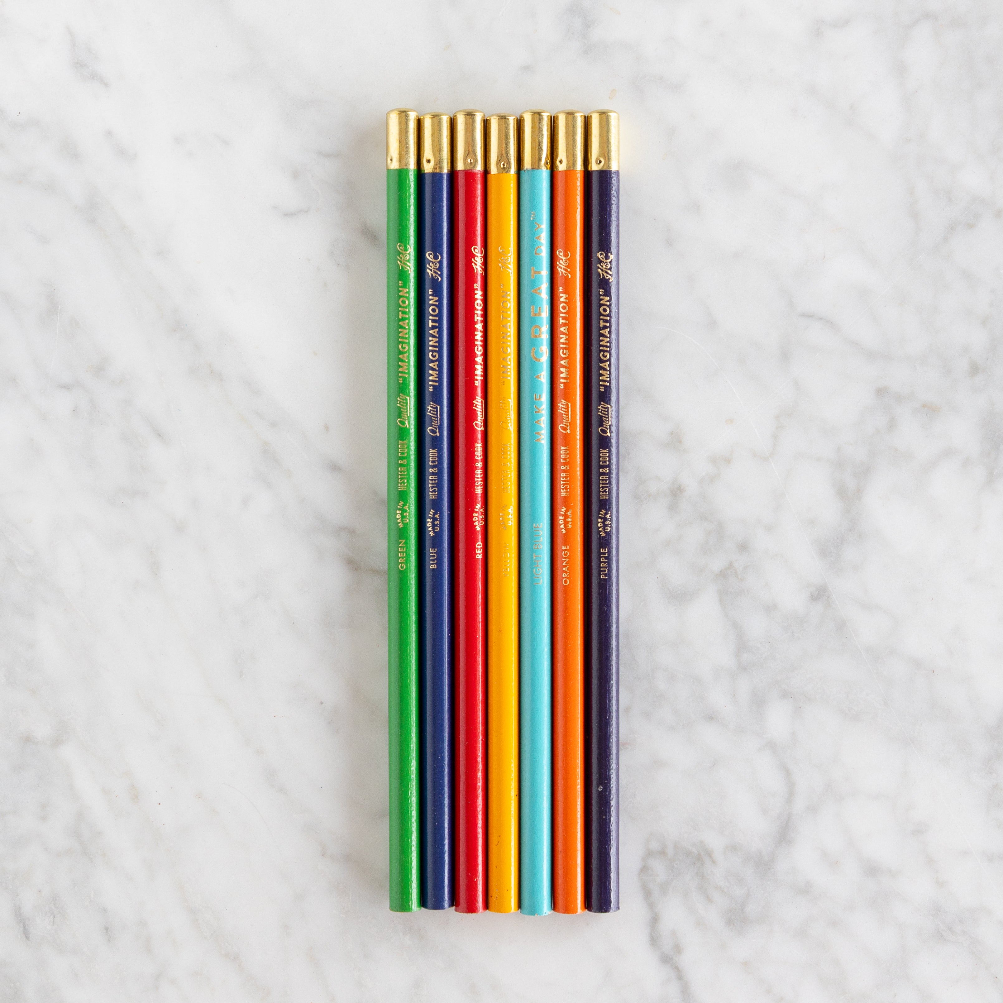 Set of colored pencils with gold caps on a marble surface.