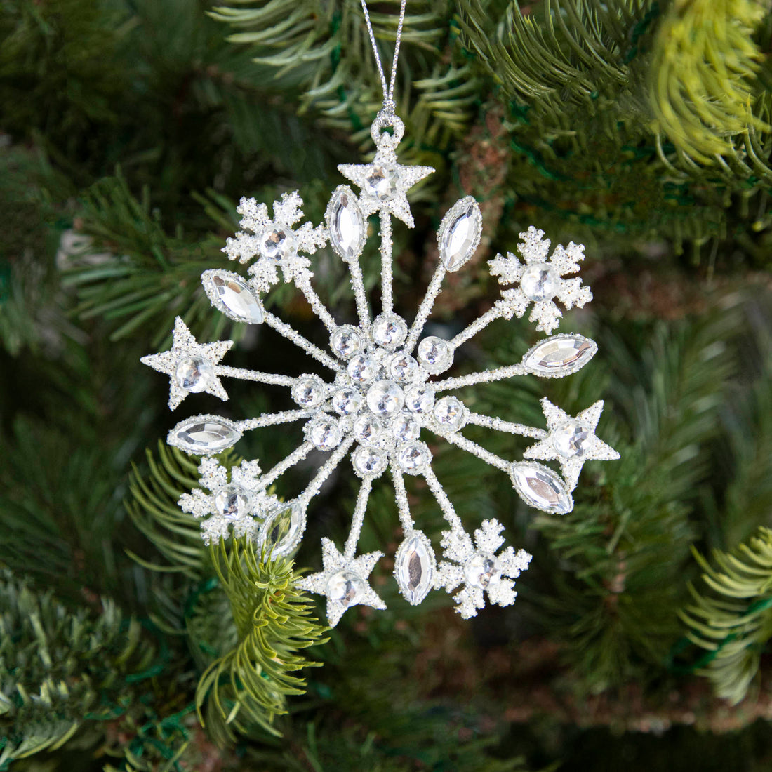 A Crystal Jeweled Snowflake Ornament hanging on a tree.