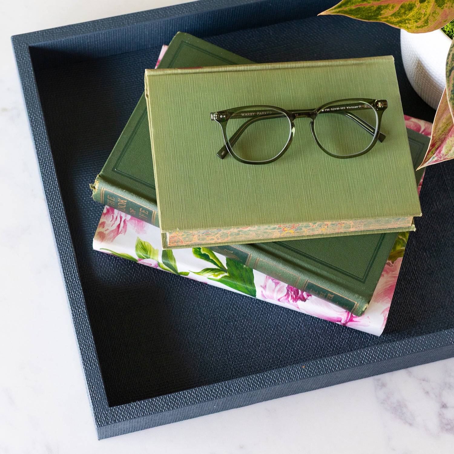 Stack of green books with a pair of glasses on top, placed on the  Indigo St. Tropez Decorative Tray. 