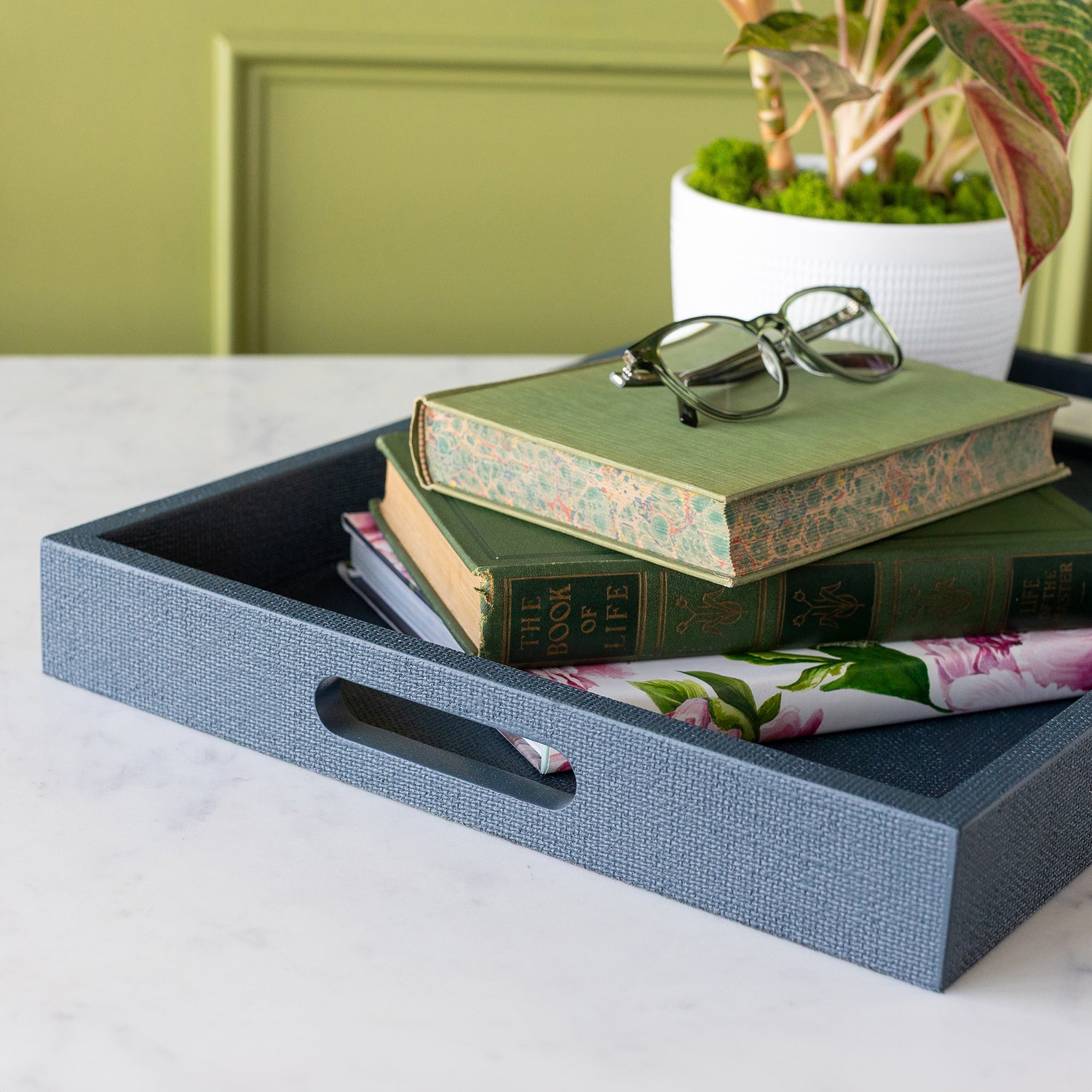 Indigo St. Tropez Decorative Tray with books, a pair of glasses and a plant atop, on a marble surface against a green wall.