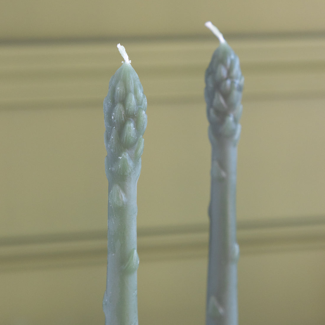 Two asparagus shaped candles on a green background.