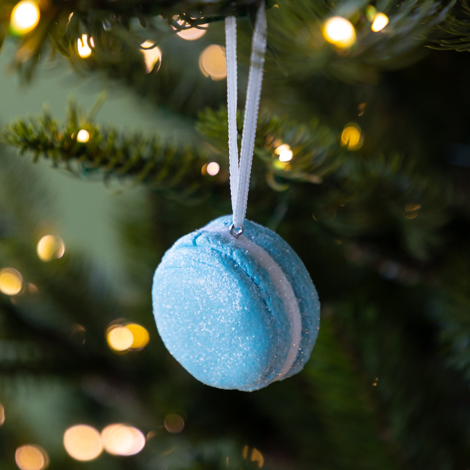 Blue macaron ornament hanging on a Christmas tree with blurred lights in the background.